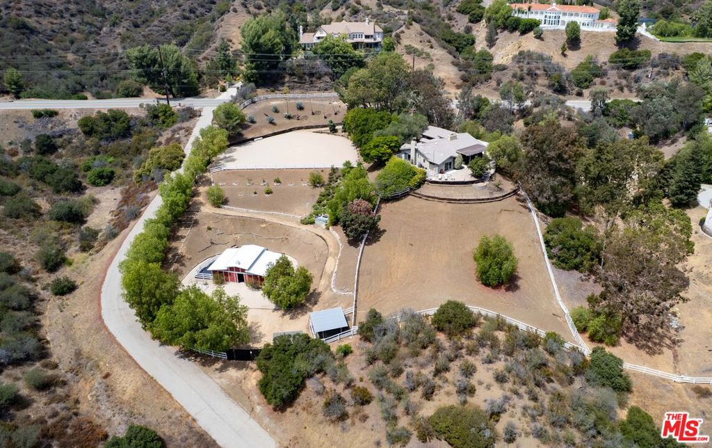 Welcome to 25700 Mulholland Highway, an extraordinary equestrian estate on nearly two acres along the iconic Mulholland Corridor in Calabasas, California. Set behind gates and surrounded by mature olive trees and sweeping views of the Santa Monica Mountains, this rare compound offers a seamless blend of luxury living and rural charm just minutes from both Calabasas and Malibu. The beautifully remodeled single-story home spans approx. 2,500 square feet and features Turkish limestone floors, soaring ceilings, and walls of glass that bring in natural light and frame panoramic views. Highlights include a formal living/media room with custom built-ins, a dramatic great room with fireplace, and a designer kitchen equipped with Sub-Zero, Wolf, and Miele appliances, granite counters, and book-matched custom cabinetry. The flexible floor plan includes two sleeping rooms on one side including a private primary retreat with walk-in closet, custom built-ins, spa bath and mountain views. Off the kitchen, an impressive executive office suite (3rd bedroom) has high ceilings, wet bar, spa bath, and its own entrance to the front courtyard. Outside, the property boasts a detached two-car garage with workshop and storage, a private state of the art movie trailer/theater, ample parking, and incredible equestrian amenities. A professionally graded riding arena, two-stall barn, and large tack room/lounge sit below the main house, connected by a private trail and peaceful waterfall feature. The property also offers a pad for an airstream, and direct access to scenic trails in the Santa Monica Mountainsperfect for morning rides. A true gentleman's ranch and one-of-a-kind offering for equestrian lovers, nature seekers, or anyone craving privacy, views, and elegant indoor-outdoor living.