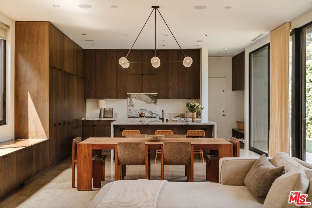 Nestled behind a veil of lush greenery, this striking residence by renowned architectural firm Marmol Radziner embodies the essence of California modernism: bold, sophisticated, and effortlessly livable. Completed in 2016, the home is a masterful interplay of refined materials, voluminous spaces, and seamless indoor-outdoor flow, offering an exceptional retreat in one of Los Angeles' most vibrant enclaves. The minimalist charcoal facade opens to interiors reminiscent of a classic Venice artist loft -- expansive, adaptable, and elegantly curated. Soaring ceilings and polished concrete floors define the main level, where a wall of sliding glass doors dissolves the boundary between the open-plan living area and the tranquil backyard oasis. The gourmet kitchen is a sculptural centerpiece, featuring solid oak cabinetry, dramatic Arabescato marble countertops, a full suite of Miele appliances, and a generous walk-in pantry equipped with a beverage refrigerator. A versatile bedroom suite on the first floor opens directly to the patio, ideal for hosting guests, establishing a home office, or cultivating creative pursuits. Upstairs, the serene primary suite features a custom oak headboard wall, dual walk-in closets, and a spa-like bath enveloped in handcrafted Heath tile. Two additional en-suite bedrooms maintain the home's minimalist aesthetic and invite natural light and treetop vistas through expansive aluminum-framed windows. A thoughtfully positioned skylight above the stairwell imbues the space with a soft glow, enhancing the architectural harmony across both levels. Balancing clean-lined simplicity with refined luxury, this residence supports a lifestyle rooted in design, ease, and connection to nature. Located just moments from the pulse of Venice, this home enjoys close proximity to the iconic Venice Beach and boardwalk, the trendsetting boutiques and acclaimed restaurants of Abbot Kinney, and a rich tapestry of neighborhood amenities that define the Westside's vibrant cultural fabric.