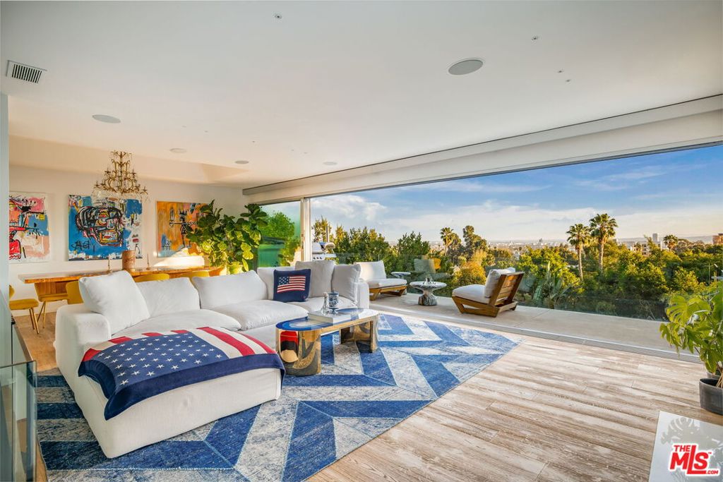 Perched on a private cul-de-sac above the Sunset Strip, this meticulously remodeled contemporary estate captures breathtaking panoramic city views. Behind a gated entry, a serene courtyard with manicured landscaping and a tranquil fountain sets the tone for refined elegance. Inside, floor-to-ceiling Fleetwood sliding glass doors frame the dazzling skyline and open to expansive view decks, creating a seamless indoor-outdoor flow throughout the main living spaces. The great room features a sleek fireplace and sophisticated wet bar, with a gourmet Miele kitchen replete with porcelain countertops, built-in breakfast nook, and uninterrupted views. The elevated primary suite is a private sanctuary complete with its own living area, oversized walk-in closet, and a spa-inspired ensuite bath boasting heated floors, a rain shower wrapped in gorgeous glazed tile, and dual vanity sinks accentuated by Calacatta marble countertops and designer brass finishes. Just outside, an in-ground spa with cascading waterfall and fire features provides the perfect setting for relaxation or entertaining. Additional highlights include a versatile first-level bedroom or office with views and garage access, and a separate private studio space with its own direct entrance - ideal for guests or creative use. The entertainer's backyard offers multiple seating areas, a fire pit, and a dramatic outdoor dining space designed to maximize the glittering city vistas that define this one-of-a-kind Hollywood Hills estate.