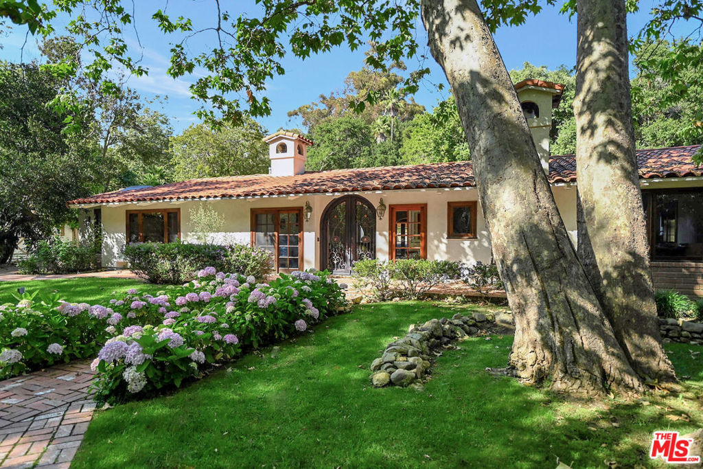 This magical 1.3-acre Spanish-style estate offers a serene escape in Ramirez Canyon, one of Malibu's most private, gated communities. Nestled amongst majestic oak trees and a babbling creek, this hidden gem provides unmatched tranquility just minutes from Paradise Cove Beach. The single-story home features a grand formal living room with vaulted ceilings and a cozy fireplace, flowing seamlessly into a gourmet kitchen with a spacious island and dining area with an additional fireplace. The primary suite boasts three closets and two beautifully appointed bathrooms, one with a steam shower and the other with a clawfoot tub beside a fireplace for relaxation. Three additional bedrooms and two flexible spaces accommodate a variety of lifestyle needs. Expansive windows throughout the home showcase manicured grounds, a private citrus orchard, and multiple entertaining areas, including a large patio, flat grassy lawns, a pool, spa, and a newly built glass-and-steel greenhouse. As a valuable bonus, the home is equipped with a full-house generator, ensuring uninterrupted comfort. This estate offers the perfect balance of seclusion and convenience - a rare opportunity in Ramirez Canyon.