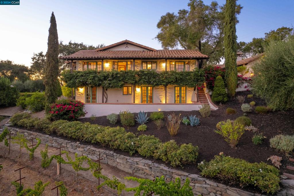 Secluded behind a private gate on 1.71 acres of beautifully landscaped grounds, this Monterey Colonial Hacienda is a private oasis just minutes from town. Built in 1940, the estate blends timeless elegance with modern conveniences. Upon entry, you'll be captivated by its charm and seamless indoor-outdoor flow. The formal living room, dining area, and office all feature French doors that open to enchanting patios. At the heart of the home is the expansive kitchen and great room, designed for family living and entertaining. The kitchen includes a large walnut-topped island, built-in refrigerator and freezer, two dishwashers, and a fireplace. The bedrooms are equally inviting. The primary suite offers beamed ceilings and glass doors to a wisteria-covered balcony with stunning views. Upstairs, two additional bedrooms each have their own unique charm, while a fourth bedroom downstairs provides privacy and versatility. Outside, the grounds are equally captivating, with patios for al fresco dining, a sparkling pool, bocce court, firepit, and tranquil fountains. Surrounded by working grapevines and olive trees, this estate offers an ideal setting for a relaxed yet luxurious lifestyle. Located conveniently close to town, BART, the freeway and Orinda's top rated schools.