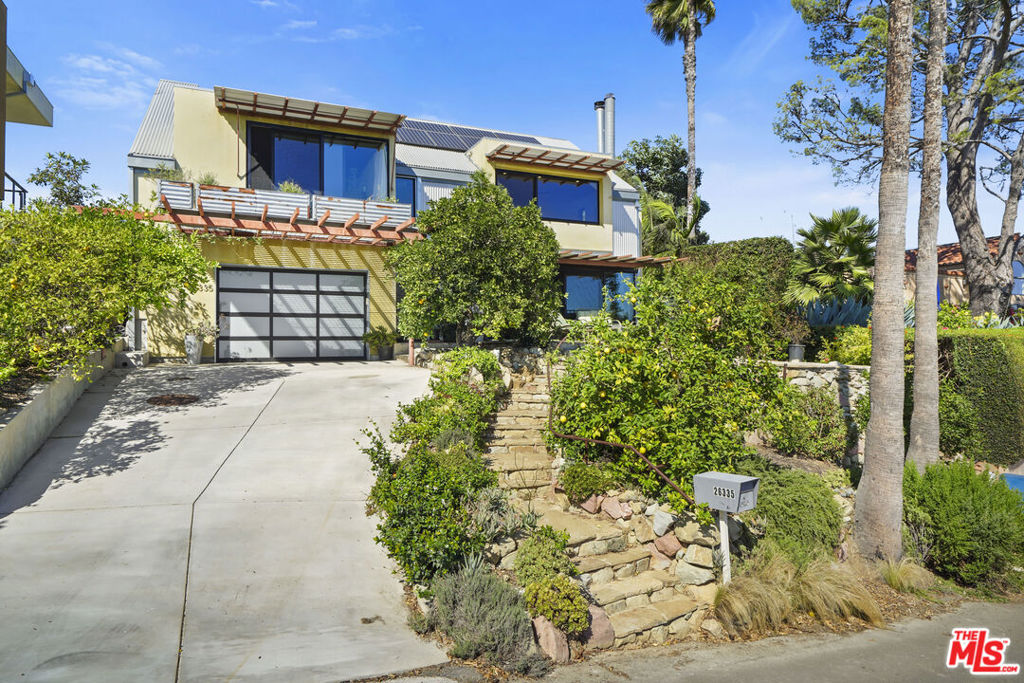 Welcome to Lockwood Road in Malibu, where contemporary design meets sustainable living. This warm modern home showcases sweeping views of the Santa Monica Bay, city lights, and Catalina Island from every front-facing room, while the Santa Monica Mountains create a dramatic backdrop out back. Crafted with intention, the residence blends wood, metal, and eco-friendly materials for an ergonomic and environmentally conscious design. The flexible floor plan includes two bedrooms plus an office or third bedroom and a 12 x 25' attic loft, featuring polished concrete and cork flooring, metal accents, and a sleek stainless-steel kitchen. Floor-to-ceiling views invite natural light and create an ever-changing panorama that captivates the senses. Private front, rear, and rooftop decks provide multiple vantage points to soak in the scenery from ocean sunrises to mountain sunsets making the home as inviting outdoors as it is inside. Sustainability is at the core of this home, with solar panels, Tesla backup batteries for seamless energy use, and rainwater collection to nourish the abundant fruit trees and gardens. A rare opportunity to enjoy modern Malibu living with a self-sufficient edge.