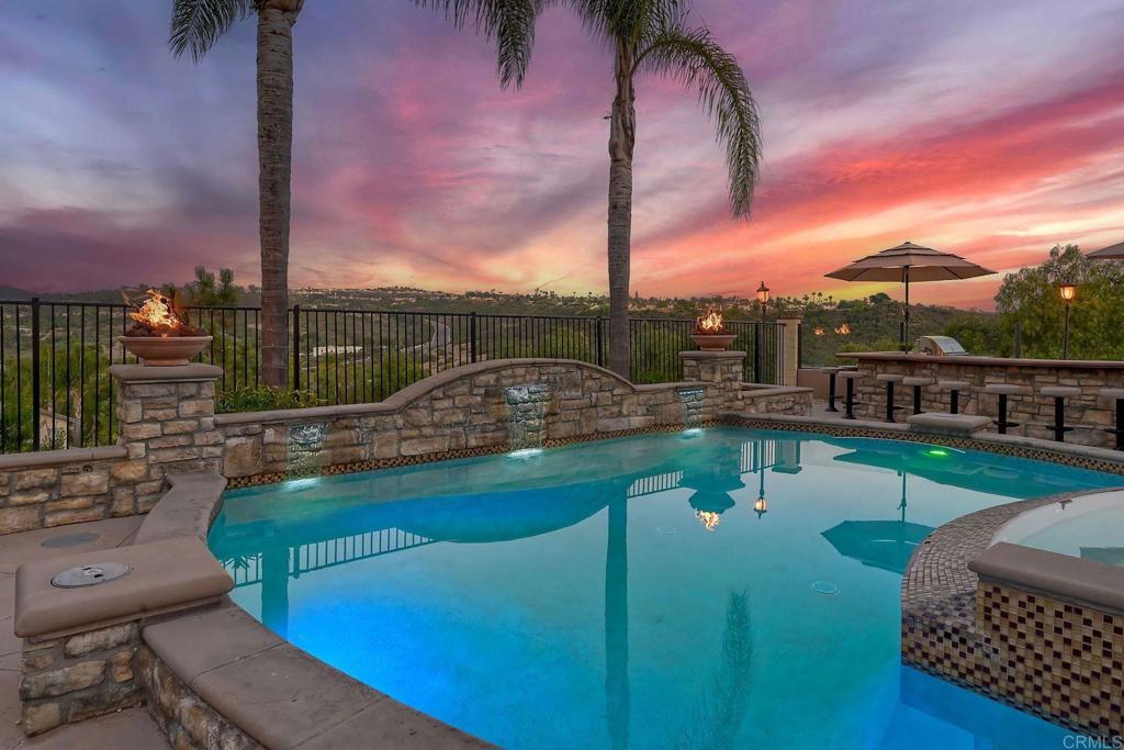 Don't Miss This Breathtaking Bressi Ranch Corner Lot Home with Views, Luxury Features, an Entertainer’s Dream Backyard & PAID Solar! Inside, this stunning five-bedroom, 4.5-bath home offers soaring ceilings & expansive windows bathing the home in natural light. Step into your personal resort-style backyard, complete w/ an oversized pool & spa featuring shooting fountains, waterfalls & dramatic lava pits. The expansive outdoor kitchen seats 15—perfect for entertaining. For quieter moments, unwind in the serene courtyard around a fire w/ tranquil water features. A welcoming living room greets you upon entry w/ a cozy fireplace & French doors that open to the peaceful courtyard. Along the entry hall, you'll find the DOWNSTAIRS en-suite bedroom before arriving at the elegant dining room, which boasts a butler’s pantry & a built-in wine rack. The heart of the home is the chef’s kitchen, beautifully appointed w/ an oversized island & high-end appliances. It includes a Fisher & Paykel 6-burner range w/ double ovens & Sub-Zero refrigerator/freezer & rich cherry wood cabinetry w/ granite countertops. The kitchen flows seamlessly into the spacious family room w/ a raised-hearth fireplace & stunning views of the rolling hills & the resort-like backyard. Upstairs, discover a versatile built-in office nook & a generous loft—ideal for teens or tots. The oversized luxurious primary suite is a true retreat, featuring panoramic views & an absolutely dream-worthy walk-in closet. The en-suite bath includes his-&-hers vanities & a soaking tub w/ scenic views. Also upstairs are three additional bedrooms—one w/ its own en-suite & two others, generously sized. Located just minutes from Bressi Village's shops & restaurants & only a short drive to Carlsbad’s beaches, this exceptional home offers a vacation lifestyle.