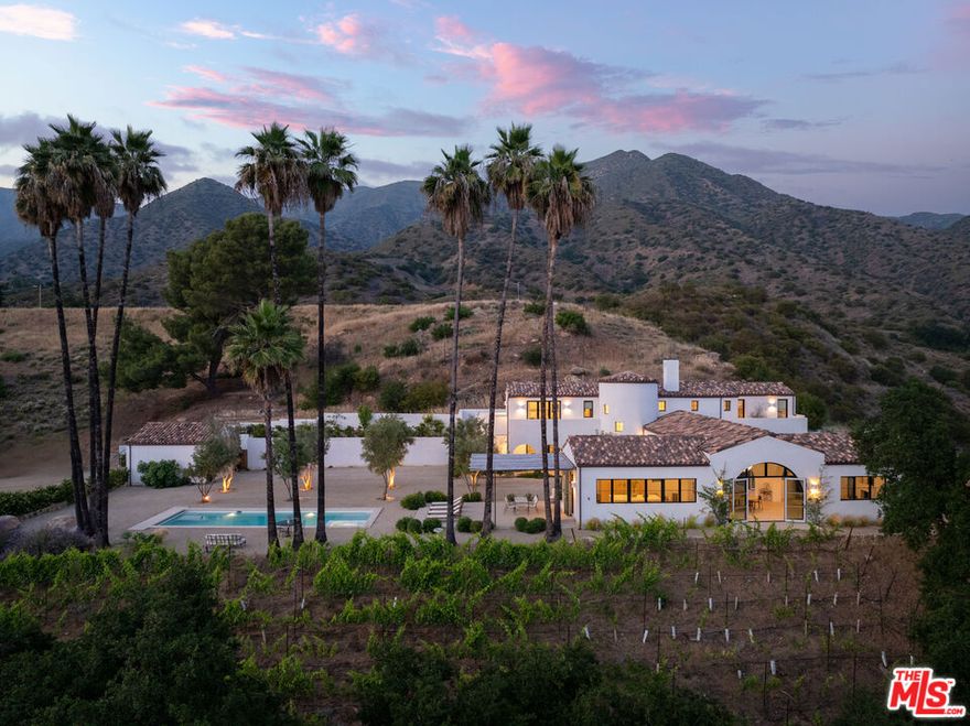 Perched on a private knoll in Ojai's coveted East End, this 2023-built estate blends modern Mediterranean design with refined living. The 5,100 sq ft villa sits on nearly two secluded acres and includes a fully licensed, organically farmed boutique vineyard with over 1,300 mature vines.Thoughtfully crafted with top-tier materials, the home features a dramatic great room with 12-foot ceilings, floor-to-ceiling French doors, groin-vaulted ceilings, and a sculptural circular staircase. White cement floors, hand-plastered walls, and arched passageways add timeless elegance.Designed for both entertaining and everyday luxury, the chef's kitchen boasts Sub-Zero refrigeration, Fisher & Paykel ovens, and Waterworks fixtures, flowing into open dining spaces and a veranda perfect for enjoying Ojai's "Pink Moment" sunsets.Four private bedroom suites, each with spa-style baths and outdoor terraces, provide serene retreats. The grounds offer ancient oaks, an olive allee, drought-tolerant gardens, a heated pool, spa, and multiple outdoor living areas.This estate combines beauty with function. Plans for an ADU, a potential winemaking facility, and safety features like fire-resistant materials, private hydrant, and emergency turnaround ensure long-term peace of mind.A rare blend of design, nature, and opportunitythis East End estate is more than a home; it's a legacy.