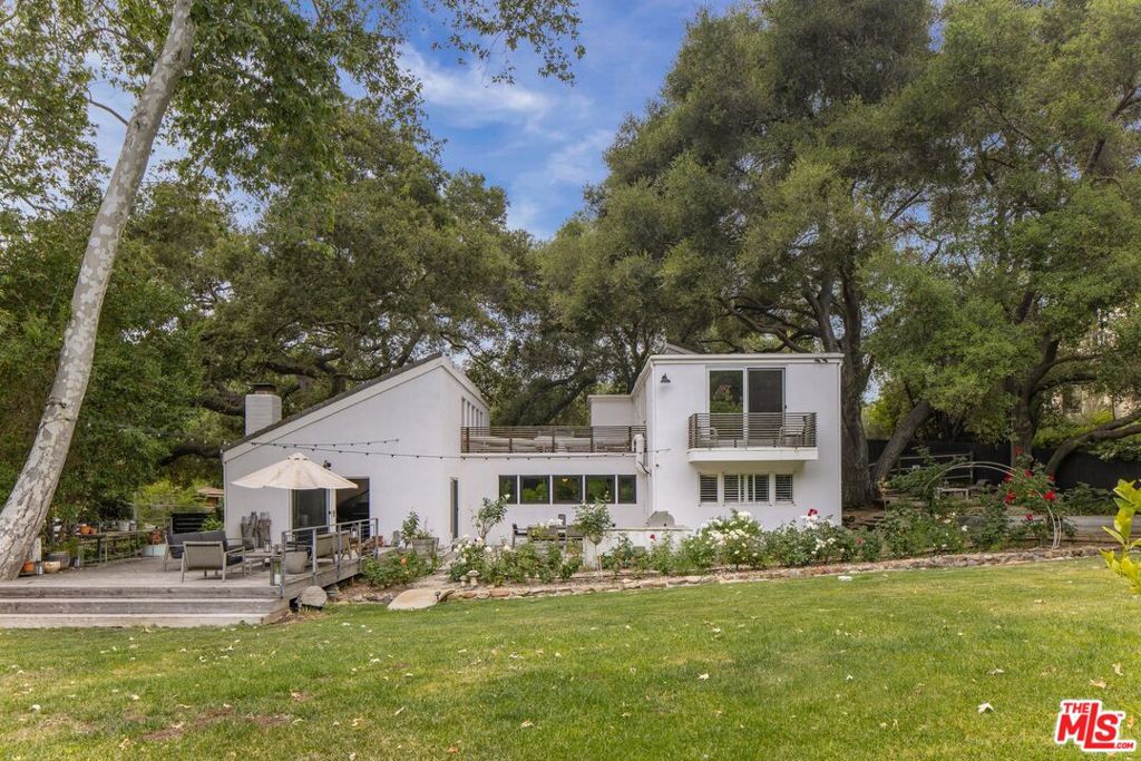 Nestled within a canopy of old-growth oaks in Monte Nido, this sunlit compound channels the quiet magnetism of Malibu Canyon with the style and sophistication of California's architectural lineage. Set across an acre of gated, verdant grounds, the home and its two curated outbuildings offer a rare canvas for both creative flow and laid-back retreat. A compelling blend of scale, natural light, and organic textures, the main residence spans 3,122-square-feet, comes fully furnished, and showcases soaring vaulted ceilings, wide-plank wood flooring, and expansive picture windows that infuse the interiors with a distinctive airiness. The spacious living room is crowned by rustic beams and anchored by a stone-clad fireplace, with warm textures and sculptural lighting that nod to a modern ranch vernacular. The adjacent chef's kitchen is flanked by a wall of windows overlooking the deck and outfitted with stone countertops, premium appliances including a double-oven range and wine fridge, and a seated center island for convenient entertaining. Upstairs, the tranquil primary bedroom offers a true sense of retreat, with lush treetop views from a balcony and a generous walk-in closet, as well as hallway access to a luxurious bathroom with a glass-enclosed shower and soaking tub positioned to catch the light. A laundry room with storage and two secondary bedrooms and bathrooms complete the layout. Sliding glass doors throughout open the home to its multiple outdoor living areas where every path invites pause: the gravel lounge nook shaded by twin oaks, a sun-washed entertaining deck, and saltwater pool and spa. Citrus trees, lavender, and a seasonal creek form a living backdrop -- lush, unforced, and ever-changing with the seasons. Off the pool deck is a fully detached studio, serving versatile space for work, artistic pursuits, or entertaining. Just beyond is a private infrared sauna, an outdoor shower, putting green, and sport court. Whether soaking beneath the stars or simply lounging on the sun deck enveloped in birdsong and breeze, this is a setting that invites a slower tempo. Supremely positioned in the Monte Nido enclave just minutes from Malibu and Calabasas proper, surrounded by trailheads and wildlife, 959 Crater Oak is a place to live, work, and create among an enchanting natural setting.