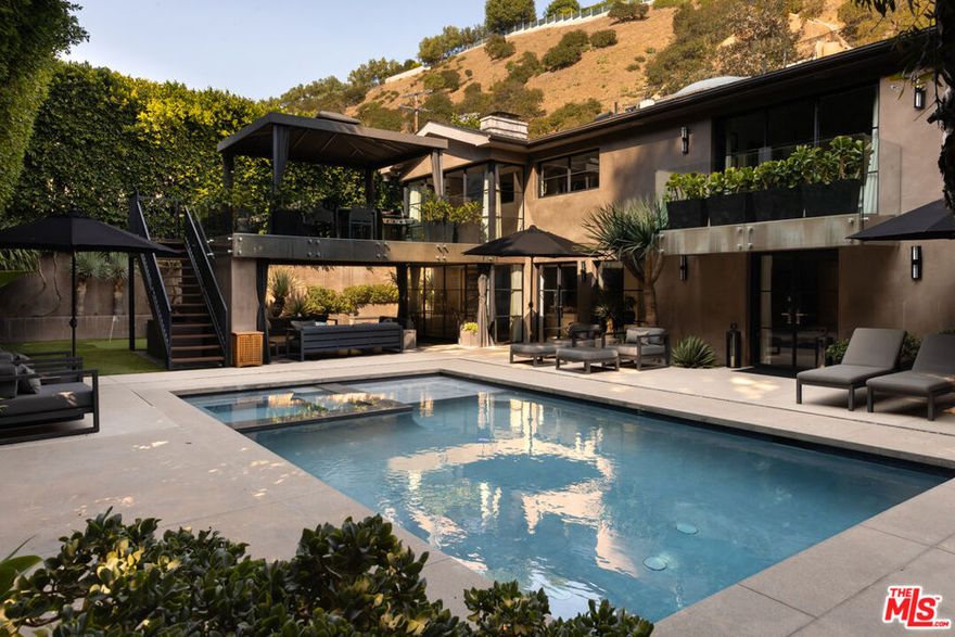 Expertly renovated and discreet Beverly Hills oasis offering high design, state-of-the-art amenities, and the serenity of canyon living. Private and peaceful, the 3 bedroom, 4.5 bathroom home sits at the top of Franklin Canyon, completely gated and landscaped to perfection, surrounded by mature plantings and hedging. With soaring vaulted ceilings, two covered patios, a home gym, and an awe-inspiring backyard with pool, firepit, and putting green, the property offers extensive amenities and effortless indoor/outdoor flow. Just a short distance from the iconic Beverly Hills Hotel and moments from Franklin Canyon Park's hiking trails, the home delivers a rare combination of privacy, nature, and proximity to the city's best offerings. Upon entry, the breathtaking open living space greets its entrants, with wide-plank oak flooring, vaulted ceilings, and gorgeous steel windows offering hillside views and abundant natural light. The airy living room is anchored by a sleek fireplace and flows seamlessly into the dining area and chef's kitchen. Outfitted with new top-of-the-line Viking appliances, custom cabinetry, and a generous peninsula with bar seating, the kitchen was designed for both culinary creativity and effortless entertaining. A wet bar features a Monogram wine/beverage refrigerator and additional storage with picture windows overlooking the striking backyard. Custom windowed French doors open to an upper covered patio, ideal for grilling and dining al fresco in the gorgeous hillside surroundings. Down the hall, find two upstairs bedrooms, including the luxurious primary suite, complete with a large, outfitted walk-in closet and a private balcony with windowed French doors overlooking the canyon. The perfectly appointed, spa-inspired bathroom features a striking marble dual-sink vanity, water closet, soaking tub, and large walk-in shower with dual showerheads. Descend to the lower level, where a second open-concept living space awaits, complete with a bar, corner office space, powder room, and a den with French doors leading to an intimate covered patio. The lower level is the ultimate space for recreation and relaxation, featuring an additional bedroom with an ensuite bathroom, laundry room, and gym. The gym and laundry room have the potential to be converted into an additional bedroom and bathroom, respectively - a flexible space to suit its next owner's needs. Outside, the landscaped backyard is a haven for entertaining and relaxation alike, surrounded by mature ficus hedging and expertly curated landscaping. A large pool and spa are complemented by a covered patio with an outdoor fireplace, an ideal space for relaxation and entertainment. For added leisure, enjoy a private putting green tucked among the greenery, with an adjacent seating area around a fire pit. Smart-home technologies include a built-in Sonos sound system, Nest thermostats, and robust security systems. Upgrades include whole-house alkaline water filtration and a HEPA-equipped HVAC system. Situated in one of Los Angeles' most coveted enclaves, the property is within minutes of Beverly Hills' best destinations, including Croft Alley, the Polo Lounge, Wally's, and Rodeo Drive's world-class shopping. Offering tranquility at home and excitement just beyond your doorstep, this Franklin Canyon escape is truly the best of both worlds.