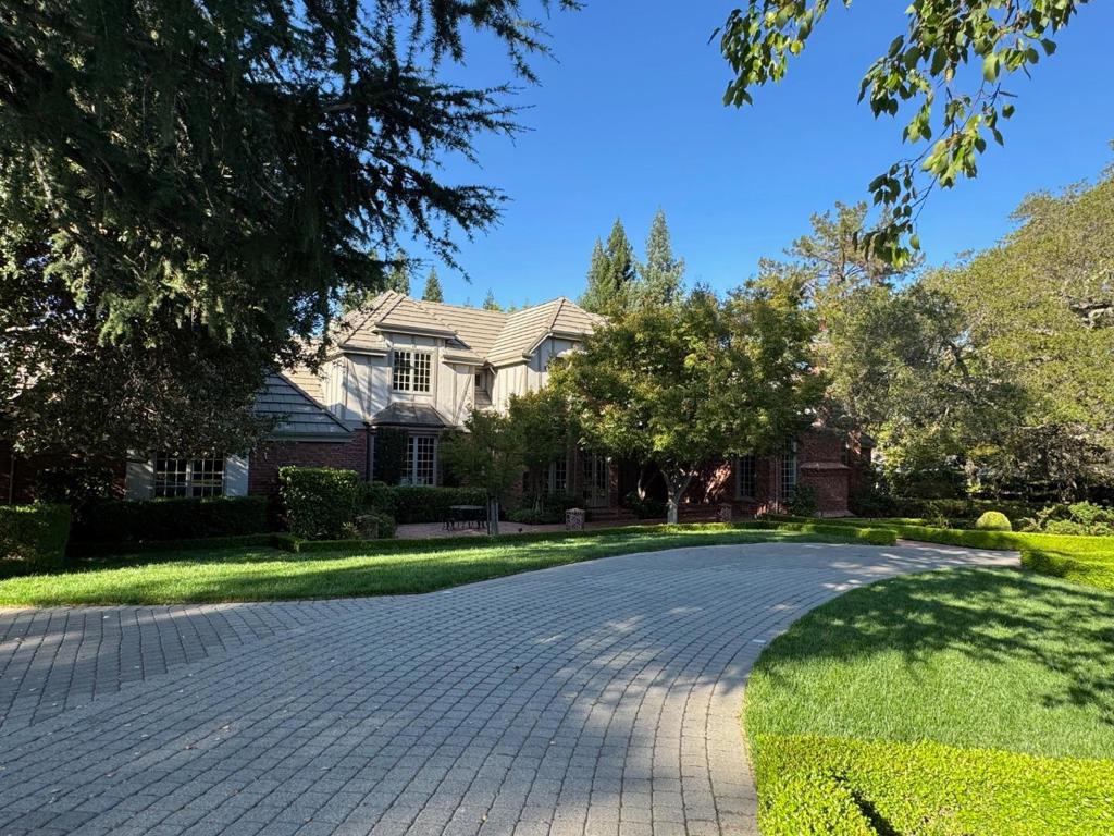 Set behind gates on one of Saratoga's most sought-after streets, this remarkable estate exemplifies timeless architectural design and quality. With its stately brick façade, grand scale, and meticulous proportions, the residence is luxurious, commanding, and private. A soaring two-story entry foyer with a custom staircase makes a striking first impression, leading to expansive, beautifully composed living spaces. Natural light flows through large-scale rooms, each thoughtfully framed to balance volume and intimacy. The opulent living room with coffered ceilings features a marble fireplace imported from Europe and opens to a richly appointed office. The first floor includes an elegant primary suite, formal dining room, and flexible bonus room offering both purpose and retreat, while the chef's kitchen overlooks the backyard and opens to the great room. All four bedrooms and five bathrooms are arranged to ensure calm and privacy, while refined materials and craftsmanship reveal the care behind every detail. Beyond the architecture, the grounds unfold with quiet grandeur: manicured gardens, a sparkling pool, vast lawns, and sweeping outdoor spaces that seamlessly extend the interiors. Mature landscaping envelops the property, offering both beauty and seclusion.