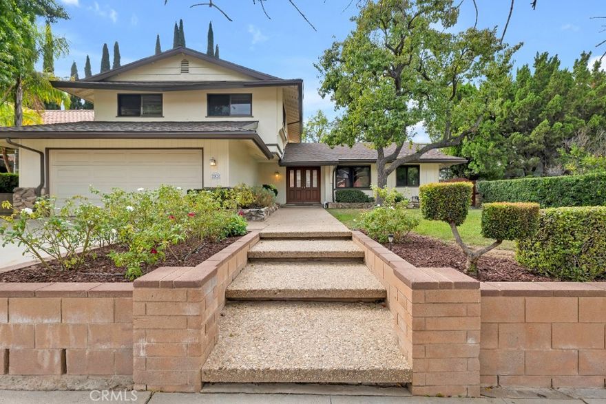 Wonderful 5-bed, 3-bath home with 2,450 sq ft of living space, perfectly positioned in a desirable neighborhood with a stunning mountain backdrop. Great curb appeal with distinctive wood siding and stone details, lush green lawn, hedge borders, and mature shade trees.  A welcoming double-door entry, accented by decorative glass, opens to a formal tiled entryway with decorative tile rug. The interior is freshly painted throughout and sets a bright and move-in-ready tone. A large, open-plan living space is filled with natural light from floor-to-ceiling windows while a statement fireplace anchors the generous living room, which flows effortlessly into the adjacent dining area with a glass slider that leads to the backyard. The kitchen combines classic function with modern updates and an inviting atmosphere, offering granite counters, a tile backsplash, and stainless-steel appliances including a built-in oven and microwave, and a cozy breakfast nook for informal dining. Two downstairs bedrooms, which share a well-appointed full bath, both with mirrored closets, one with a glass slider out back, offer flexibility, creating opportunities for a home office, guest suite, or conversion into a spacious den or bonus room. Upstairs, the primary suite features dual closets, an en-suite ¾ bath with dual sinks, a separate vanity area, and a tiled shower. Two additional good-sized bedrooms with mirrored closets share a full hall bath. Outside, the yard makes the most of the over 8000 sq ft lot with a wide concrete patio, a covered seating area, and an expansive lawn bordered by mature landscaping, creating a perfect canvas for outdoor gatherings or personalization. The home boasts an attached 2-car garage, with brand new garage door opener and laundry hookups.  Well situated in the foothills of Porter Ranch, near highly rated schools, parks and natural spaces, shopping, dining, and entertainment. Don’t miss out on this home with exceptional potential in an outstanding setting.