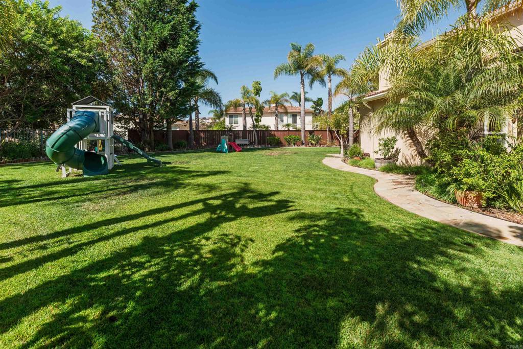 Expansive Cul-de-Sac Lot in Calavera Hills’ Capistrano Neighborhood Set on one of the largest and most distinctive lots in Calavera Hills, this immaculate home enjoys a spacious, flat pie-shaped yard at the end of a quiet cul-de-sac—a rare find in North County. Nearly a quarter acre, the backyard unfolds as a private oasis with lush tropical landscaping, a palapa designed for year-round entertaining, and abundant space to add a pool or expand outdoor living. Fully fenced and grassy, the grounds feel serene and inviting, framed by sweeping easterly views. Inside, soaring 25-foot ceilings and abundant natural light create an open, airy feel from the moment you walk in. Just off the main entry, a private main-level guest bedroom and half bath adds convenience and flexibility for guests. The formal living room, surrounded by walls of windows and high-placed glass, connects to the dining room, while sliding doors directly across open to a private side courtyard patio for an inviting extension of the main living spaces. Beyond, the kitchen and family room create a true open-concept living area. Warm wood cabinetry, a large pantry, and a butler’s pantry provide everyday function, while high-end Viking and GE stainless steel appliances add chef-level appeal. Sliding glass doors extend the space outdoors for seamless entertaining, and an extended breakfast nook makes casual dining effortless. Upstairs, the primary suite feels retreat-like with sliding glass doors to a private balcony, a huge walk-in closet, and an ensuite bath with dual sinks, a soaking tub, walk-in shower, and natural stone finishes. Two additional bedrooms share a jack-and-jill bath with an upstairs laundry room rounding out the desirable layout. Additional highlights include dual-zoned A/C, custom paint throughout, and a three-car garage. Tucked away in a peaceful Calavera Hills cul-de-sac, the Capistrano neighborhood combines a serene setting with unbeatable convenience. Families enjoy award-winning schools—Calavera Hills Elementary, Calavera Hills Middle, and Sage Creek High—all just minutes away. Scenic trails around the Calavera volcano are close by, and when you’re ready for the coast, it’s a straight shot to Carlsbad Village and the beach for dining, shopping, and sunsets.