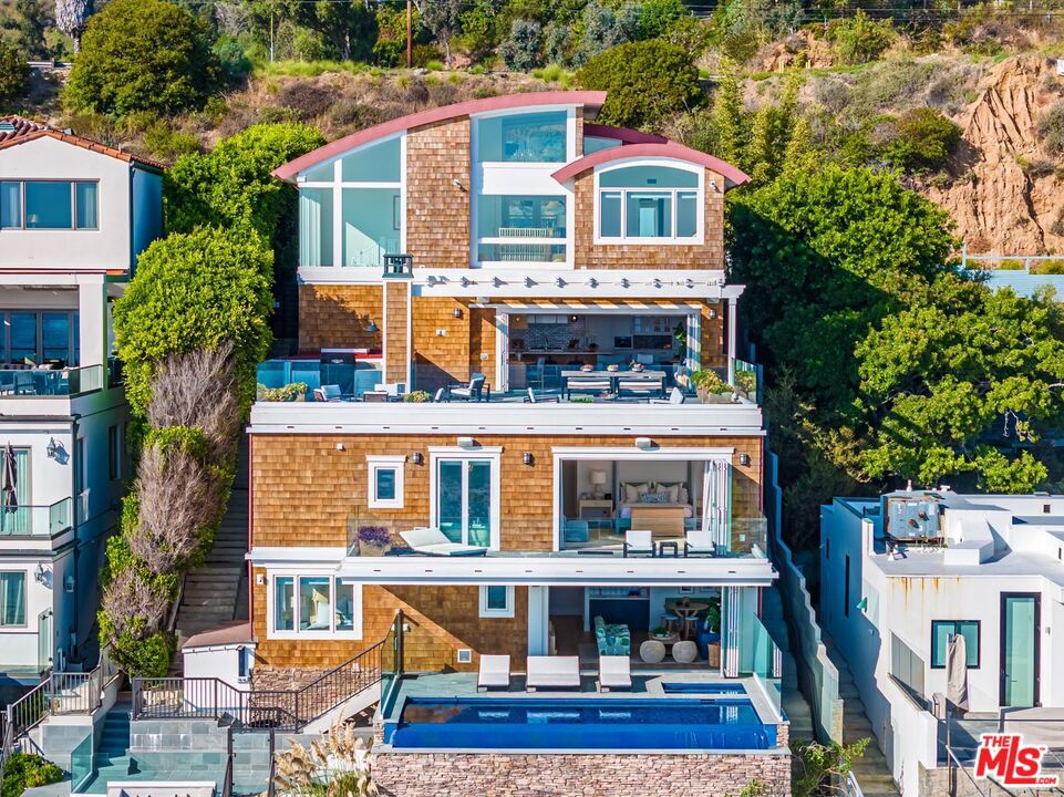 Bright multi-tiered Broad Beach home with spectacular ocean-facing terraced vistas throughout. Extensively and recently remodeled with high end, designer done quality. The property features an open layout, hotel grade amenities, high ceilings and vast windows with a bold curvilinear roof-top beautifully offset with warm redwood shingles. The street-level entry, flanked with vast transoms, houses an en-suite bedroom, and gym or additional garage parking. One level down, the great room includes a formal sitting and dining area, pristine wood beamed chef's kitchen with custom teak and marble island, all opening to an oversized flagstone deck with a wood-burning fireplace. An oversized en-suite guest bedroom completes this level. Step down to the owner's suite, with private whitewater view deck, dual baths with walk-in showers and ample closets. This level includes a den/office, state of the art home theater and well oriented laundry room. The lowest level is designed for entertainment featuring a huge media room with eating nook, wet bar and partially covered ocean-view deck with an infinity pool and spa that leads directly to the dry, sandy beach, plus three additional bedrooms. The property includes an elevator that serves all levels and off-street parking for six cars. A truly Incredible home on a coveted deep and sandy beach!