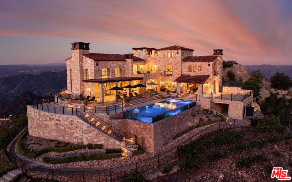 LUXURY PRIVATE AUCTION. This property is being offered via luxury private auction. Submit offers now through October 30th. Seller may accept or reject bids at any time. Visit Paramount Realty USA's website for full terms and details. Set high above Malibu's celebrated wine country, Rocky Oaks Estate crowns more than 37 acres of rolling vineyards and dramatic canyon ridges, offering an extraordinary blend of privacy, grandeur, and natural beauty. Approached through stately wrought-iron gates and a sweeping driveway, the residence occupies a commanding knoll with uninterrupted vistas stretching from the Pacific Ocean to the surrounding mountains. Designed by acclaimed architect Bob Easton, AIA, this Tuscan-inspired villa spans over 7,600 square feet and is finished in timeless stonework that evokes European craftsmanship. Inside, soaring ceilings, walls of glass, and refined proportions create a setting that is both elegant and inviting. A dramatic great room with a cathedral ceiling and monumental fireplace flows effortlessly onto expansive terraces that frame the panorama. The formal dining room, professional-grade chef's kitchen with butler's pantry, and multiple gathering areas make the home ideal for both intimate living and grand entertaining. The primary suite is a private retreat with its own terrace and fireplace, spa-inspired bath, and dual dressing rooms, while three additional guest suites, staff quarters, and a media room ensure comfort for family and visitors. An elevator, three-car garage with ample guest parking, and a rooftop observation deck offering 360-degree views elevate the lifestyle experience.Outdoors, the estate is a sanctuary of leisure and beauty. Wraparound loggias with fireplaces, a dining pavilion, an infinity-edge pool and spa, and a circular observation pad invite year-round enjoyment of Malibu's climate. Nearly five acres of the estate are dedicated to the Rocky Oaks Vineyard, established in 2003 and now one of the most renowned vineyards within the Malibu Coast American Viticultural Area. Producing award-winning varietals recognized for their exceptional quality, the vineyard carries forward a legacy of winemaking that dates to the early 1800s in this region. Rocky Oaks Estate is more than a residence- it is a landmark of architectural vision, viticultural excellence, and Malibu prestige, awaiting its next discerning steward.