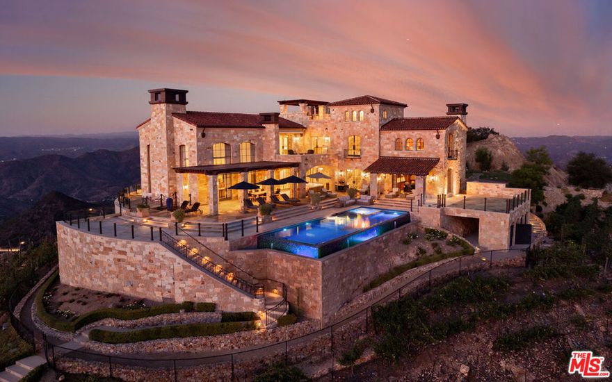 LUXURY PRIVATE AUCTION. This property is being offered via luxury private auction. Submit offers now through October 30th. Seller may accept or reject bids at any time. Visit Paramount Realty USA's website for full terms and details. Set high above Malibu's celebrated wine country, Rocky Oaks Estate crowns more than 37 acres of rolling vineyards and dramatic canyon ridges, offering an extraordinary blend of privacy, grandeur, and natural beauty. Approached through stately wrought-iron gates and a sweeping driveway, the residence occupies a commanding knoll with uninterrupted vistas stretching from the Pacific Ocean to the surrounding mountains. Designed by acclaimed architect Bob Easton, AIA, this Tuscan-inspired villa spans over 7,600 square feet and is finished in timeless stonework that evokes European craftsmanship. Inside, soaring ceilings, walls of glass, and refined proportions create a setting that is both elegant and inviting. A dramatic great room with a cathedral ceiling and monumental fireplace flows effortlessly onto expansive terraces that frame the panorama. The formal dining room, professional-grade chef's kitchen with butler's pantry, and multiple gathering areas make the home ideal for both intimate living and grand entertaining. The primary suite is a private retreat with its own terrace and fireplace, spa-inspired bath, and dual dressing rooms, while three additional guest suites, staff quarters, and a media room ensure comfort for family and visitors. An elevator, three-car garage with ample guest parking, and a rooftop observation deck offering 360-degree views elevate the lifestyle experience.Outdoors, the estate is a sanctuary of leisure and beauty. Wraparound loggias with fireplaces, a dining pavilion, an infinity-edge pool and spa, and a circular observation pad invite year-round enjoyment of Malibu's climate. Nearly five acres of the estate are dedicated to the Rocky Oaks Vineyard, established in 2003 and now one of the most renowned vineyards within the Malibu Coast American Viticultural Area. Producing award-winning varietals recognized for their exceptional quality, the vineyard carries forward a legacy of winemaking that dates to the early 1800s in this region. Rocky Oaks Estate is more than a residence- it is a landmark of architectural vision, viticultural excellence, and Malibu prestige, awaiting its next discerning steward.