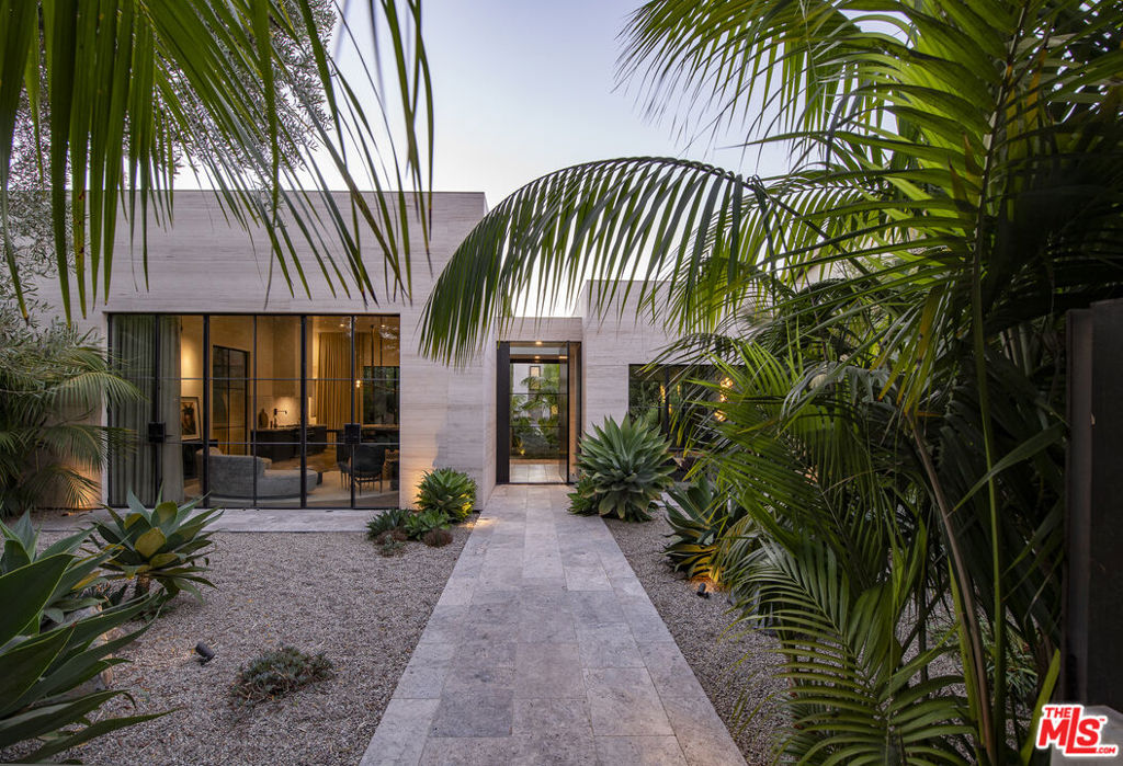 Discover an unparalleled Modern Hacienda-style compound inspired by Venice's rich artistic heritage. Completed in 2020 by acclaimed architecture and design firm Electric Bowery, with landscape design by Terremoto, the residence comprises a main home and a versatile guest house on an expansive 10,415 square-foot lot. Enveloped by luxuriant grounds and secured behind gates, the compound was designed to blur the lines between interior and exterior living spaces through the continuous use of natural materials like limestone and vein-cut travertine. Featured in Architectural Digest Latin America, the visionary residence is meticulously curated for a bold, yet tranquil living experience emphasizing natural light, unique textures, and luxurious finishes. Enter the main residence through a dramatic foyer, where the eye-catching turquoise-plastered walls of the media lounge is to the right, and the great room with a gourmet kitchen featuring a Lacanche range and family room with a bar is on the left. Ideal for lavish entertaining and everyday living, the great room is flanked by floor-to-ceiling steel-framed doors that showcase picturesque garden views. Bespoke millwork in oak with an indigo-ebony finish and sculptural lighting by Apparatus Studio anchor the space, while whole house automation by Control4 allows residents to conveniently command the ambiance with the touch of a button. Traverse the gallery to enter the primary wing, where each detail was thoughtfully considered to create a haven of comfort. Here, find two custom walk-in closets, an ensuite with a skylight-lit rain shower and dual vanities, and generous sleeping quarters. Meandering pathways through the lush landscape travel by water features, a Japanese copper cold plunge, an outdoor shower, multiple patio spaces including one set around an outdoor wood-burning fireplace beneath a retractable canopy, and the handcrafted-tiled pool/spa. Completing the awe-inspiring experience is a versatile guest house or artist's studio with a secondary suite, living space, office, and yoga studio with radiant heated floors and a state-of-the-art sauna. Attached to the guest house is an oversized three-car garage with ample storage space. Crafted for those seeking a creative retreat in one of LA's most vibrant artistic communities, this residence affords the opportunity to live in a home where every architectural angle sparks creativity, every material tells a story, and inspiration flows as freely as the California sunshine.