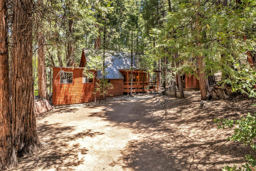 IDYLLWILD CLASSIC ON SEASONAL CREEK Rich wood paneling, open beam ceilings and original custom craftsmanship and finish, highlight this beautifully maintained Fern Valley home in a picturesque creek setting with lemon lilies. A spacious great room has a stunning floor to ceiling native stone fireplace with airtight wood stove insert, authentic arts & crafts period lighting and multiple picture windows to enjoy views of the surrounding landscape. The charming kitchen boasts handcrafted cabinetry, open shelving and original wood countertops. A separate dining room with cathedral ceiling, has walls of windows with private views and a custom natural edge aspen dining table from Colorado. There are 2 bedrooms, including large upstairs open beam primary bedroom with bay window, 1.75 baths and a cozy den with built-in cabinets and shelving plus a separate office area. There is also laundry with washer/dryer, forced air heat, metal roof, covered front deck, large rear deck with hot tub and a spacious detached studio/workshop with wood stove.