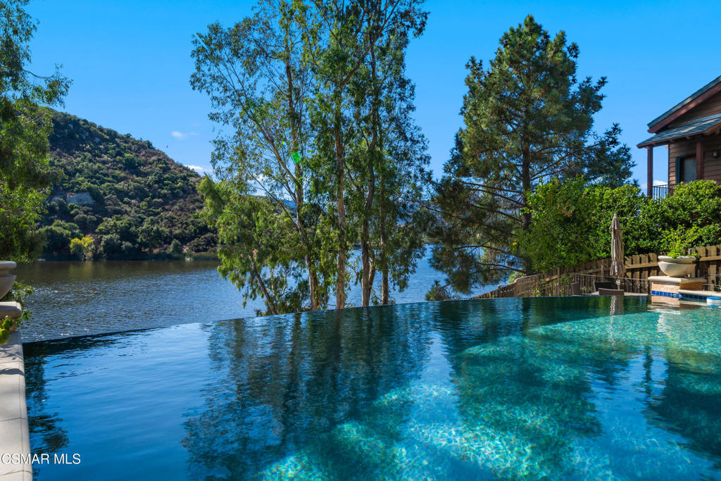 Discover perfection at Lake Sherwood with this extraordinary lakefront home, beautifully remodeled to showcase expansive views of Lake Sherwood and the protected Santa Monica Mountains. Every detail has been thoughtfully curated to offer the ultimate in lakeside luxury, with a smart home system, a private deep-water dock, a gated front yard, a resort-style pool and spa with all-day sun, and impeccable hardscaping and landscaping throughout.Step into the main floor's grand living space, where a great room with floor-to-ceiling glass doors blurs the line between indoor and outdoor living. Elegant rustic white oak floors and a dramatic stone fireplace create a warm and inviting atmosphere, while the spacious bar area, formal dining room, and chef's kitchen--featuring top-of-the-line Thermador Professional Series appliances, including a 48'' range with griddle, three ovens (two gas with the range and one built-in electric baking oven with warming drawer and microwave), and an expansive 72-inch refrigerator and freezer setup--complete this refined space. The kitchen has been custom-built and remodeled, including a beautiful table that seats up to 10. The primary suite, also on the main level, features a cozy fireplace, dual walk-in closets, and a luxurious bath with Carrara marble finishes. A versatile guest bedroom or office rounds out the main floor.The lower level offers an expansive family room with a fireplace, three additional bedrooms (including one ensuite), and three separate decks designed for seamless entertaining. Enjoy the convenience of a pool bathroom and outdoor shower on the bottom deck, along with a fire pit for cozy gatherings with panoramic lake and mountain views year-round. The upper deck boasts a built-in BBQ, a covered and heated, glass-enclosed sitting area with a TV and electric screens to shield from sunlight and keep warmth in on chilly evenings. A motorized full-size awning covers the outdoor dining area for additional comfort.Outside, this lakefront retreat is an oasis of natural beauty, with a spacious backyard drenched in sunlight from morning till dusk, a delightful rose garden that blooms year-round, and a perfect view of sunsets to the west. Located in the premier part of the lake, this property invites you to embrace a vacation lifestyle every day, with private access to boating, swimming, fishing, and paddleboarding.Just minutes from Westlake Village's vibrant amenities, the exclusive Sherwood Country Club, top-rated schools, and Malibu's beaches, this tranquil sanctuary is perfectly situated for the best of California living.