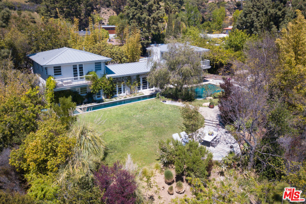 Magnificent gated contemporary home by Paul Hinckley. Organically infused materials such as glass, wood & concrete are used throughout the house creating a gorgeous light-filled oasis. The open entry leads to a living room w/soaring Douglas Fir ceilings, two-sided wood burning fireplace & concrete style floors. The private dining room contains the same surfaces as the living room, creating a seamless visual experience. Stunning chefs kitchen with stainless steel appliances. There is a large meditation/spa room with a luxurious indoor/outdoor bath area. The master suite is located up a private mahogany staircase with sumptuous master bath, walk-in closet and French doors that lead out to a romantic balcony. There are four additional bedrooms and an office. All public rooms lead to a gorgeously landscaped outdoor area with an exquisite lap pool, spa, bbq and enormous grassy yard with unique views that overlook Lake Hollywood Reservoir and the City. A rare offering.