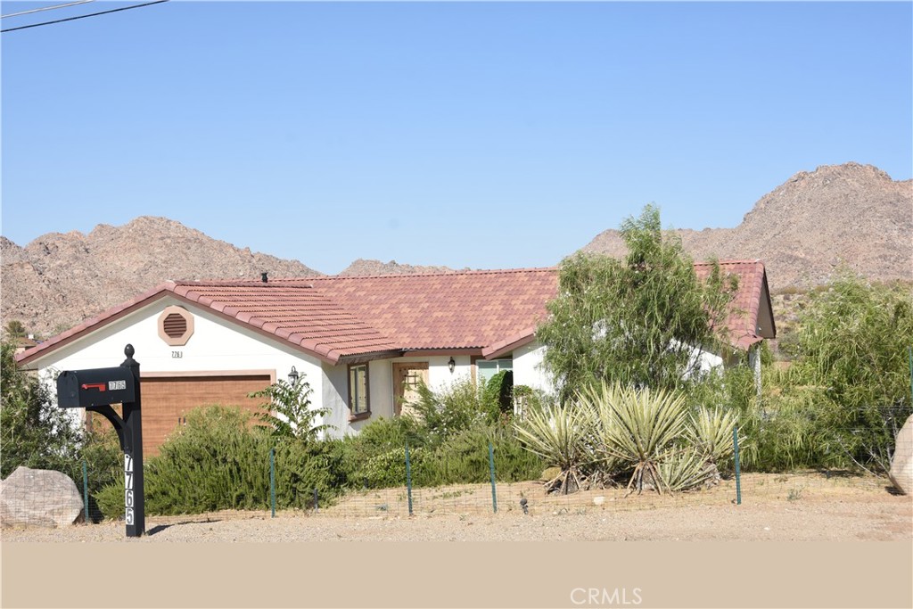 This corner lot property boasts stunning and unobstructed views of Joshua Tree National Park, situated south of Highway 62. It features a complete underground sprinkler system that covers the entire lot, and underground power instead of traditional overhead power. The property has never been lived in, and is adorned with mature trees such as a Santa Rosa plum tree, three fruitless mulberry trees, three umbrella trees, and several popular trees. The landscaping also includes plenty of agave and other plants, with fencing in place to protect them from wildlife. The backyard features a custom block stucco wall and a drainage ramp to channel any excess water off the property. Low voltage lighting illuminates the plants, landscaping, and walls at night. The home includes a new stainless steel counter depth refrigerator, honeycombed energy efficient pleated shades for window coverings, stucco eaves for low maintenance and fire protection, and a tile roof with low attic vents for a streamlined appearance. There are three large bedrooms, including an extra large master suite on the opposite side of the home from the other bedrooms. The master suite has two sinks, a Kohler soaking tub, a separate walk-in shower with a seat, and Arizona subway tile installation. The master closet is a walk-in with a Martha Stewart wooden organizer and exclusive higher-end ceiling fans are found throughout the home. The outdoor LED ceiling fans in all rooms are by Casa Delta-Wing and have oil-rubbed bronze finish motors with solid wood walnut finish blades, integrated opal glass light 12 W LED modules, and hand-held remote controls. Each bedroom also includes a closet organizer with shelving and shoe storage, and the kitchen has an island with hanging lights above it. The countertops are made from Arizona granite from a slab yard out of Anaheim, and feature a unique styled tile backsplash that goes up behind the stainless steel hood. Stainless steel appliances include a higher-end GE Profile 5 burner cooktop, top-of-the-line microwave and oven combination, dishwasher, and a hood by ANCONA ELITE WPE630.