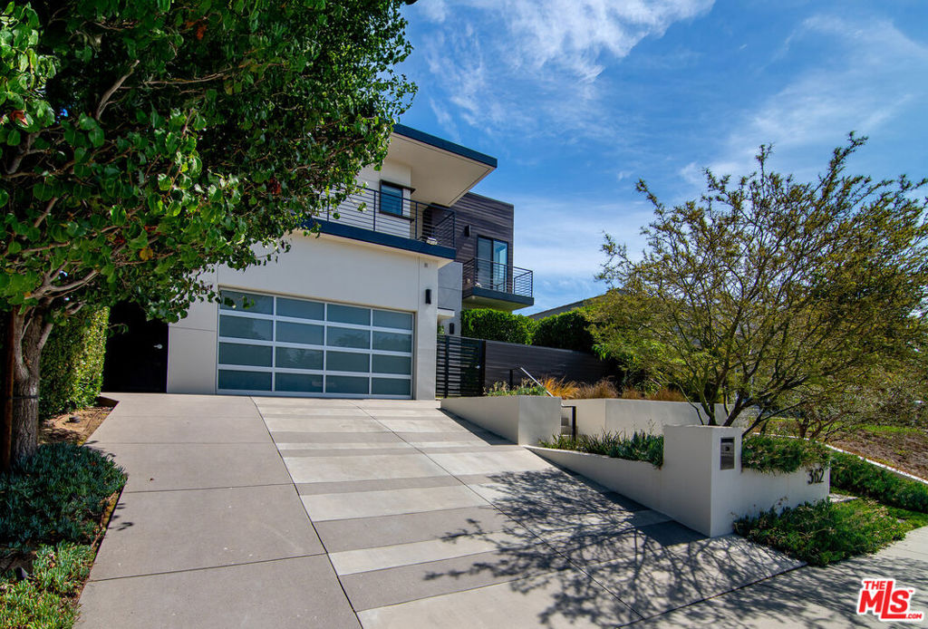 Sophisticated Contemporary in the Heart of Larchmont Village. Perched gracefully above the street, this striking contemporary home blends modern design with high-end finishes, creating a private sanctuary in one of the city's most sought-after neighborhoods. Walls of glass and soaring ceilings bathe the interiors in natural light, while seamless indoor-outdoor flow connects open living spaces to an inviting courtyard and the expansive rear garden. The main level offers a spacious open floor plan with living, dining, and a chef's kitchen featuring Miele appliances, a convection oven, center island with breakfast bar, and generous storage. A flexible den/guest quarters with built-in seating/storage and adjacent full bath, along with direct interior access from the two-car garage, complete the level. Upstairs, three bedroom suites each enjoy their own private patios. The primary retreat overlooks the gardens and boasts a custom walk-in closet and a spa-like bath with dual sinks, a soaking tub, and separate water closet. In addition, there is a bright open space, ideal as a study, gym, or additional lounge. A full laundry room rounds out the upper level. Set on one of the largest lots in Larchmont Village, the home is designed for entertaining with a built-in outdoor barbecue and multiple spaces to gather, relax, and unwind. Just blocks from Larchmont's beloved boutiques, cafes, and the twice-weekly farmers' market, this home offers both tranquility and vibrant neighborhood living.