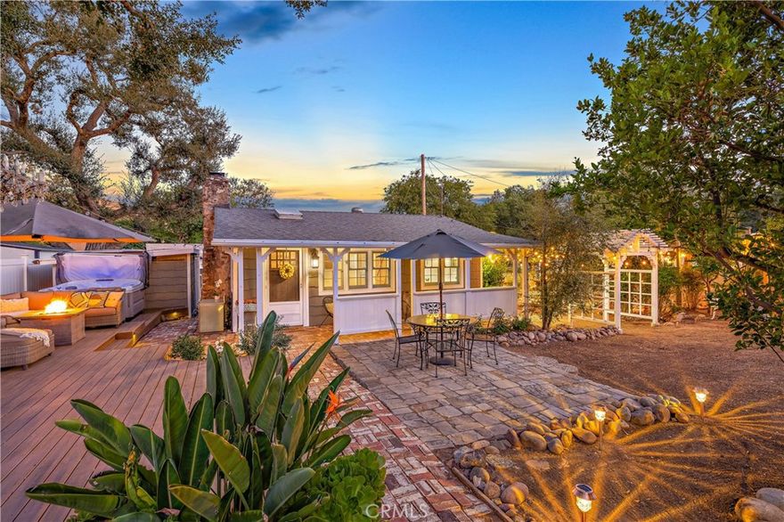 Situated on a spacious, level, double lot, this enchanting country retreat invites you to relax and enjoy life’s simple pleasures. With plenty of room for gardening, pets, and even RV parking, this turnkey home has it all. Inside, the living room features a vaulted ceiling, multiple skylights, wood flooring, a dining area, and a cozy river rock fireplace with a wood-burning stove for maximum heat efficiency. The main bedroom offers tumbled marble flooring, and an attached full bathroom with a large tub and tiled surround. The smaller second bedroom or office showcases a beautiful farmhouse-style barn door and enjoys views of the front yard. The upgraded kitchen includes a garden window overlooking the scenic grounds, granite counters, a stainless refrigerator, an electric stove, and a microwave. Additional amenities include: three new mini-split heat and air units (located in both bedrooms as well as the kitchen), a separate storage garage with washer and dryer, two extra storage rooms ideal for work or hobbies, a relaxing spa, and an expansive custom Trex deck for stargazing evenings. The fully fenced grounds feature a private garden with raised planter beds, ten mature fruit trees ranging from pomegranates to tangerines, meandering brick paths covered in trellises and grapes vines, a stone patio with fire pit seating, and a concrete parking area with an electric gate for added convenience and security. Recent upgrades include dual-pane windows, fire-resistant siding, a tankless water heater, updated electrical, and wired security. Residents of this sought-after community appreciate a variety of neighborhood traditions, including the much-loved Fourth of July parade, as well as access to the community riding arena, O’Neill Park, and miles of scenic trails. Enjoy close proximity to Rose Cantina, the iconic Trabuco Oaks Steakhouse, shopping, and Trabuco Canyon Elementary- all within a top-rated school district. Full of warmth and style, this Trabuco cottage offers canyon living at its finest- come experience the lifestyle you’ve been waiting for.