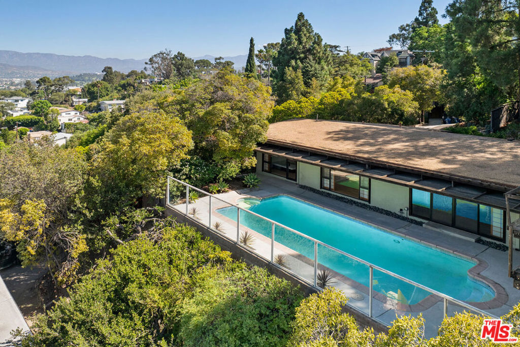 Available for lease in Silver Lake, this midcentury home with a pool enjoys rare privacy and cinematic views of the Reservoir, Griffith Observatory, the Hollywood Sign, and the surrounding hills. A serene study in Japanese-influenced design, the residence begins with a gently gurgling entry pond with waterfall, leading to open interiors with beamed ceilings, wood textures, Nelson pendant fixtures, and sliding glass doors framing stunning vistas. Light fills the interconnected living, dining, and den spaces; the bright kitchen features wood and tile countertops and a stainless appliance suite. Three bedrooms include an ensuite primary; both bathrooms are appointed with spa showers. Sliding doors extend the living space to the patio and pool, an exquisite setting for starlit dinners and leisurely afternoons. Landscaped with drought-tolerant flora, the property includes front and back yards, central air, laundry, and an attached garage. You're in the heart of Silver Lake near LAMILL, Botanica, the Reservoir, and more.