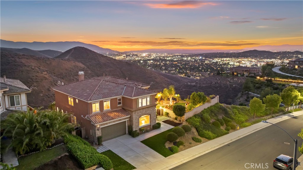 Perched on a private and premium QUARTER ACRE LOT with ONLY ONE NEIGHBOR in Lake Hills Reserve, this 4,474 SqFt residence — the one with the IN-LAW’S SUITE DOWN!! — delivers unforgettable and TOTALLY UNOBSTRUCTED CITY LIGHT AND MOUNTAIN VIEWS perfected positioned to view the setting sun seven nights a week! Designed with flexibility and comfort in mind and near the downstairs laundry room, the main floor features a private in-law suite with its own bedroom, bathroom, and retreat with room for a kitchenette —perfect for long-term guests or extended family. Speaking of kitchen, this home has a large one with granite countertops, stainless steel appliances, and an island all of which is open to the fireplace-warmed family room while the formal living and dining rooms are up front offering options to entertain in style. Upstairs offers even more room to breathe with four additional bedrooms, including two secondaries with a shared double-sink bathroom, a junior suite with its own ensuite bathroom, and then, of course, the expansive primary with its own fireplace-warmed retreat, huge bathroom with standing shower, soaking tub, and his and hers vanities as well as views all around. You’ll also find a spacious bonus room that can flex as a media lounge, home office, or even a 6th bedroom. Outside, the back and side yards are designed with peace and tranquility in mind with carefully laid out palms, a stone water fountain, gazebo-like seating area, and all with a focus on those absolutely dynamic city light and mountain views. Situated on 750 acres, Lake Hills Reserve offers its residents an ideal mountaintop locale removed from city life, yet close to the many cultural and educational amenities of Riverside County and shopping. Residents enjoy the expansive open space, the HIGHLY rated Lake Hills Elementary and a private residents club including a swimming pool, playground, park and an open-air fireplace pavilion. This is an ideal location for commuters as the 91 Freeway and Metrolink are both close by. Are you ready for the Lake Hills Reserve lifestyle?