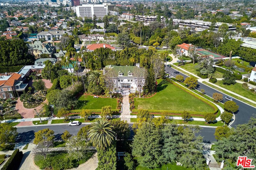Exceptional luxury and historic provenance come together in this 1915 Hancock Park estate once owned by Muhammad Ali. The property has an aesthetic gravitas worthy of its former owner, featuring a Tiffany stained glass panel and the original French Empire crystal chandeliers and fireplaces. Wood paneling, marble and hardwood floors, and large bay windows give the interior a timeless beauty. Built by John C. Austin, known for Griffith Observatory and City Hall, the estate has hosted such luminaries as Sylvester Stallone, Clint Eastwood, and President Obama. Continue the tradition of grand entertaining. Greet guests in the impressive foyer and hold court in the formal dining and living rooms. Imbibe amongst the art-filled gallery walls in the third-floor ballroom at the fully-equipped bar, before retiring to the semi-circular solarium. The grounds, occupying a desirable corner lot, are enclosed by privacy hedges, offering a lush lawn, beautiful landscaping, a swimming pool, and a terrace.