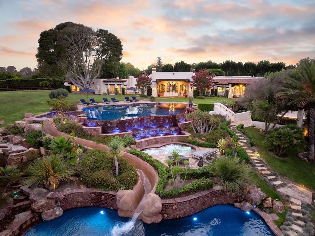 Welcome to Rancho Azul, an extraordinary custom-built estate completed in 2017 and enhanced with nearly $1 million in upgrades over the past year. Set on 3.75 serene acres in the prestigious Rancho Santa Fe Covenant, this single-level residence blends coastal Spanish influences with modern, organic design, creating a bright, modern space infused with neutral tones. The home exudes warmth and invites you to experience the vibrant energy of California living. Step outside to the resort-like grounds, where a tiered infinity-edge pool with a 75-foot water slide connects two pools, one designed as a private beach oasis. The expansive outdoor living spaces, including a sports court, children’s playhouse, and luxury glamping areas, provide the perfect setting for gatherings or quiet retreats. Nestled behind dual gates on one of Rancho Santa Fe’s most coveted streets, the nearly 10,000 sq. ft. main residence offers 4 bedrooms, each with lavish en-suite baths and seamless indoor/outdoor access. The luxurious primary suite is the ultimate retreat, featuring a sitting room/office, indoor/outdoor shower, soaking tub, sauna, cold plunge, and dual walk-in closets. Three additional bedroom suites plus an office provide privacy and comfort for family and guests. Steps away is a custom director’s theater offering the perfect spot to watch football or your favorite Netflix shows. The heart of the home is a chef's kitchen, perfect for entertaining, with a hand-carved wood island, custom cabinetry, Monte Blanc quartzite countertops, and a custom Heston convection range, combining three freestanding ranges for the ultimate culinary experience. The adjacent great room epitomizes California living with its open floor plan and seamless transitions to the awe-inspiring outdoors. Beyond the main residence, the estate includes a 2-bedroom guest house, a 3-stall barn and arena with direct trail access for equestrian enthusiasts, and meticulously landscaped grounds. This stunning estate offers both privacy and exclusivity, just moments away from top-rated schools, world-class golf courses, and upscale dining and shopping. Here, you get to live life like you’re on a permanent vacation.
