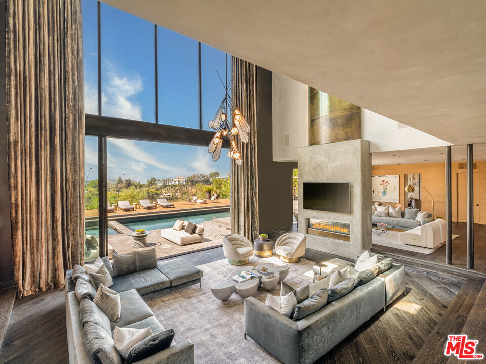 Privately gated in one of Beverly Hills' most prominent zip codes sits this contemporary architectural with exquisite detailing and comprehensive views. Remodeled in collaboration with a famed Hollywood designer and former celebrity owners John Legend and Chrissy Teigen, the residence is a celebration of comfort and opulence. Offering extraordinary scale, the home has 33-foot custom ceilings, an elegant foyer, a sunken living room and sitting room separated by a dramatic concrete and brass fireplace. The chef's kitchen features custom cabinetry, top-of-the-line appliances, and an entertainer's island with the range built in. Light radiates through floor-to-ceiling windows and a beautifully fashioned staircase leads upstairs to a collection of ensuite bedrooms plus a family room/office space with captivating views. The expansive primary suite connects to a personal glam room and bespoke showroom-style closet. Every amenity is accounted for including a full-sized gym and an upscale home theater. With an assortment of comfortable gathering spaces, the sociable backyard completes the home with a relaxing heated pool, jacuzzi and outdoor kitchen. Serenely secluded and situated on 0.86 acres, this home is the gold standard for luxury living with convenient access to the best of Beverly Hills.