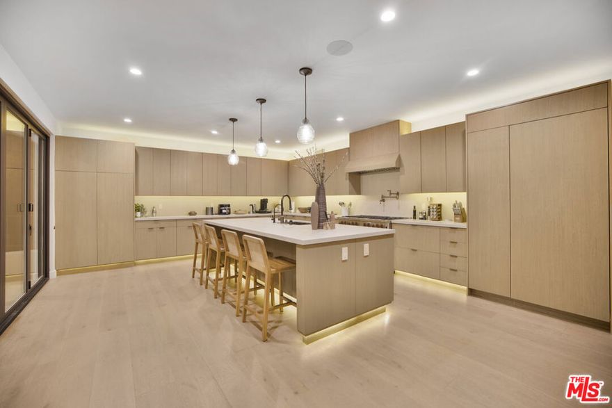 A newly built contemporary Mediterranean compound in the Hollywood Hills with sweeping views of Los Angeles and SoFi Stadium. Celebrity-owned, this property combines modern luxury with natural elegance. The open floor plan features a spacious living and dining area that flows into a gourmet kitchen with custom cabinetry and sliding glass doors leading to a large balcony overlooking the city. The nearly 2,000 sq ft primary suite includes a wet bar, Juliet balcony, fireplace, indoor/outdoor lounge, expansive bathroom, and a massive walk-in closet. The lower level offers a theatre, office with a view, wellness area with a sauna, massage space, and gym. The backyard is designed for entertaining, complete with a pool, spa, outdoor bar, fire pit, and BBQ area. Additional features include smart home technology, gated parking for four cars, and a three-car attached garage. Located near Runyon Canyon and minutes from Hollywood and Studio City, Villa de Vistas offers premier amenities and panoramic views in one of LA's most desirable settings.