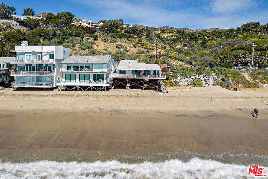 YES, ALL THAT BEACH TO THE SIDE IS YOUR PRIVATE BEACH. . . . . . . . . This rare offering on Malibu Road boasts approximately 300 feet of total ocean frontage and sits on over an acre of land, combining a beautifully renovated beachfront home with the adjacent vacant lot for unmatched privacy and scale. Fully furnished and move-in ready, the residence features vaulted ceilings, rich hardwood floors, and panoramic views from nearly every room. A wraparound deck and direct beach access make indoor-outdoor living effortless, ideal for relaxing or entertaining. The open-concept kitchen flows seamlessly into the dining and living areas, highlighted by a floor-to-ceiling stone fireplace and sliding glass doors that frame the Pacific. The primary suite offers a king bed, walk-in closet, and spa-like bathroom, while the guest suite enjoys its own ocean views and private bath. Automatic window treatments and high-end appliances elevate the experience. The expansive land next door, included in the sale, offers an extraordinary opportunity for outdoor entertaining, private events, or future development. A quiet stretch of sandy beach, this estate blends luxury, seclusion, and versatility. Located moments from Malibu's best dining and shops, this is coastal California living at its finest.