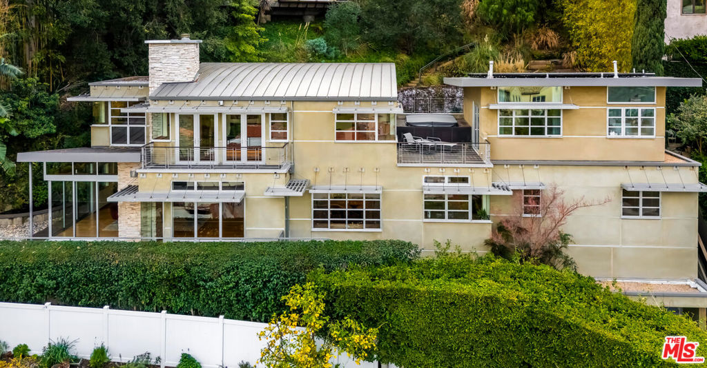 Private and serene with sweeping city views, this gated, custom modernist home in lower Hollywood Hills feels worlds away while remaining exceptionally central to the city. Designed by owner and architect Carter Bravmann, the expansive residence is poised on a terraced site of nearly 10,205 square feet that frames panoramic hill, evening-light and Downtown LA views. Nearly every room in the four-bedroom, four-bath arrangement welcomes city, hill or garden vistas, with a blend of floor-to-ceiling and clerestory windows allowing natural light to bathe living areas in a warm and inviting glow. The free-flowing two-level floor plan of approximately 3,816 square feet offers public spaces for entertaining and relaxation on a virtually seamless first floor, where the living room and den showcase a vaulted wood ceiling and stone fireplace. A built-in window seat enhances the dining room, which continues to a chef-inspired kitchen with custom wood cabinetry, an island with prep sink, granite countertops, high-end stainless-steel appliances, and French doors leading to the backyard. An ensuite bedroom on this level also opens to the backyard, and the versatile family room can be enjoyed as a fourth bedroom with private bath. Upstairs, guests will appreciate a private suite with impressive views and access to an adjacent deck. The primary suite's two balconies captivate the eye with the iconic views you'd expect in the Hollywood Hills. The main bedroom has a sitting area with fireplace. A barrel ceiling finished with natural wood crowns the space, which also reveals a magnificent walk-in closet with custom built-ins, and a large bath with floating vanity, two sinks, and a walk-in wet room with rain shower and tub. High ceilings continue throughout the second floor, which hosts a convenient home office. Every detail was personally selected by Bravmann, including wood flooring, a floating open-riser staircase, mitered windows for flawless views, recessed art lighting, and natural stone finishes and amenities. Virtually hidden from the street behind a gated driveway with two-car garage, outdoor spaces are embellished by lush landscaping that weaves towering bamboo and manicured vines into a front patio and a gorgeous backyard with pool. Taking its place near such esteemed landmarks as The Stahl/Case Study House 22 and Frank Lloyd Wright's Storer House, this modern architectural home is easily walkable to all things fun along the Sunset Strip, including shops, restaurants and clubs.