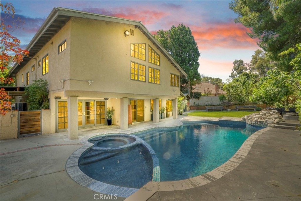 Elevated living awaits in the serene hills of Tarzana. Situated on a coveted cul-de-sac, this nearly 3,800 sq. ft. designer residence blends architectural sophistication with functional elegance.
From the moment you arrive, curated landscaping and a nearly new roof set the tone for what lies within. Inside, soaring ceilings, statement windows, and bold, artistic touches create a dramatic yet inviting ambiance. A captivating built-in aquarium divides the grand living room and fireplace lounge, creating a striking focal point.
The kitchen is a true showpiece—crafted for those who entertain with intention. Custom cabinetry, a large marble-topped island, high-end appliances, and a walk-in pantry are all framed by an expressive backsplash and vibrant finishes. Adjacent, a sunlit formal dining room sets the stage for memorable evenings.
Versatility defines the expansive layout. The large family room flows into a lower-level ensuite and an extraordinary bonus room—currently a salon—ideal as a gym, studio, private office, or guest quarters.
The upper level offers a luxe primary retreat with vaulted ceilings, a reading/office niche, three walk-in closets, and a spa-caliber bath complete with soaking tub and separate shower. An additional ensuite bedroom, two more guest rooms, and a stylish full bath complete the floor.
Outside, enjoy resort-style amenities including a sparkling pool and spa, grassy lawn, and a detached, powered structure perfect for creative or professional use.
A rare fusion of volume, vibrancy, and vision—this is more than a home; it's a lifestyle statement.