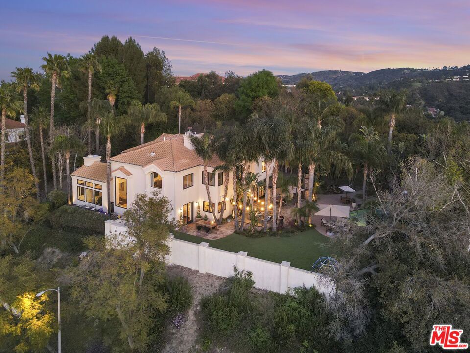 Welcome to an extraordinary estate nestled in the prestigious neighborhood, "The Heights" of Woodland Hills, where classic sophistication meets modern luxury. Set on almost an acre of sprawling, mostly flat land, this remarkable property is the epitome of privacy, elegance, and refined living. This home is perched atop hills, South of Ventura Blvd, offering unparalleled privacy and sweeping views. As you approach the property, a long, private, gated driveway leads you to a grand motor court surrounded by mature, lush landscaping and towering trees, creating a serene and tranquil atmosphere. The double-door entry opens to a breathtaking foyer and atrium, bathed in natural light from oversized windows that frame stunning views from every angle. The soaring ceilings and expansive open spaces create an immediate sense of grandeur. The formal living room exudes chic sophistication, with its inviting ambiance enhanced by exposed beams and fireplace. Adjacent to this space is a beautiful office, offering custom built-ins and a perfect setting for work or study. The formal dining room, fit for the most exquisite dinner parties, seamlessly flows to the outdoor entertaining areas. A stunning bar adds an element of glamour, while the large family room, open to the kitchen, creates a perfect gathering spot for family and friends. At the heart of the home, the chef's kitchen is a true masterpiece. Featuring a massive island, abundant storage, a walk-in pantry, and a separate coffee station, every detail has been meticulously maintained. Equipped with new, high-end Bertazzoni appliances including dual dishwashers, a sleek refrigerator, and a top-of-the-line ILVE range the kitchen is as functional as it is beautiful. A whole-house water filtration system adds an extra touch of luxury. Step outside, and you'll find a true entertainer's paradise. The expansive backyard features a fully equipped outdoor kitchen, complete with a built-in BBQ, range, warming drawer, ice maker, two sinks, refrigerator, and a pizza oven perfect for hosting gatherings. An inviting seating area comfortably accommodates guests, while the massive, lush grass area offers ample space for events, children's play, pets, or simply enjoying the outdoors in complete privacy. With breathtaking views of the surrounding landscape, this outdoor space is unparalleled. The enormous pool and Jacuzzi, complete with a built-in seating area above the Jacuzzi, provide an idyllic retreat. For added convenience, there is a luxurious guest suite located on the main floor. This private retreat is ideal for visitors, featuring a spacious bedroom, full bathroom, and easy access to all the home's primary living areas, ensuring both comfort and privacy. Upstairs, the private quarters include four spacious bedrooms, each with exceptional closet space, and two full Jack-and-Jill bathrooms. The grand primary suite is nothing short of an oasis offering a fireplace, a generous seating area, breathtaking views from every window, two walk-in closets plus a separate shoe closet, and a luxurious spa-inspired bathroom with a jetted tub, steam shower, heated floors, and majestic scenery. A Juliet balcony adds the finishing touch to this incredible retreat. This exceptional property is more than just a home...it's a lifestyle!