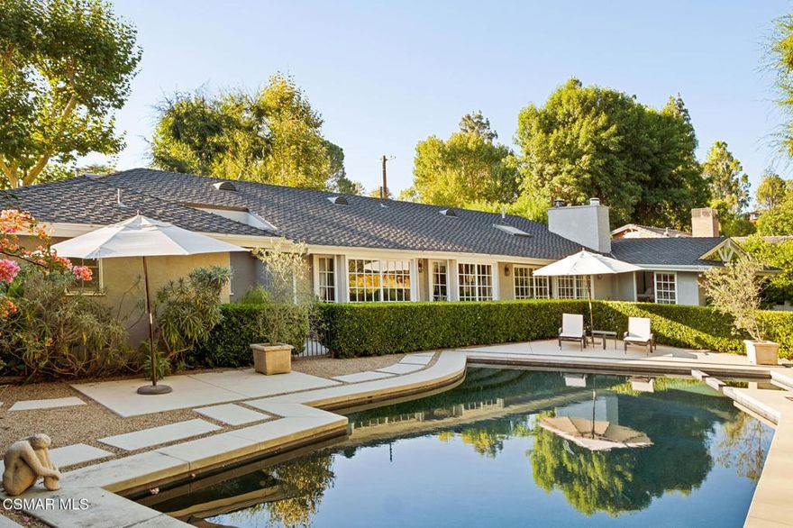 Welcome to this remarkable five-bedroom, four-bathroom California Ranch retreat, ideally located south of the Boulevard in Woodland Hills' coveted Vista De Oro neighborhood. Offering more than 3,200 square feet of timeless living space, the home is surrounded by mature trees and lush landscaping. A classic facade, double-door entry, and gracefully designed garden pathways create an inviting first impression. Inside, the design emphasizes comfort, flow, and enduring style. The primary suite is a one-of-a-kind retreat, blending luxury with warmth. A wall of library-style built-in bookshelves brings character, while an exquisite wood-and-marble fireplace serves as a striking focal point. Classic French doors open to the outdoors, creating a light-filled indoor-outdoor experience. Overhead, oversized skylights flood the space with natural light, making the suite an inspiring sanctuary. The retreat is complete with a walk-in closet featuring custom built-ins and a spa-like bathroom with a marble soaking tub, glass shower, and dual vanities. Three additional bedrooms share a hallway bathroom, while a large en-suite bedroom at the end of the hall enjoys its own private courtyard with views of the pool--ideal for guests or extended family. A convenient powder room is also located off the main hallway. Throughout the home, classic details shine: rustic wood floors, custom built-ins, multiple fireplaces, and abundant natural light. Skylights are thoughtfully placed, enhancing the bright and airy feel while highlighting the timeless finishes. The family room flows seamlessly into the formal living and dining areas, creating connected spaces ideal for entertaining or everyday living. For the wine enthusiast, a custom climate-controlled wine cellar offers floor-to-ceiling storage for a curated collection, while the adjoining wet bar provides an elegant space for serving beverages and cocktails and also added storage. Outdoors, the backyard is designed as an extension of the home. The expansive outdoor pavilion with a wood-burning fireplace overlooks the pool and spa, while a spacious lawn and decomposed granite area provide versatility for gatherings, outdoor dining, lawn games, or play. Mature trees and lush landscaping enhance the setting, with the sparkling pool and spa serving as the centerpiece for relaxation. This residence embodies classic California Ranch living with timeless quality--from its welcoming curb appeal to its light-filled interiors and resort-style grounds. It is a truly special property you won't want to miss.