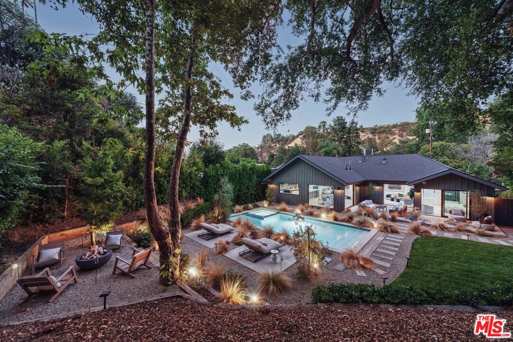 A crisp contemporary farmhouse on a sensational park-like flat lot, fully reimagined with over 3,400 square feet and finishes that sparkle from the moment you enter. From the open concept public spaces, your eye moves past floor-to-ceiling sheets of glass and ultra-wide Fleetwood doors to the resort-style yard with broad patios, deep sylvan plantings, flat grassy play areas, and a large swimming pool and spa. The main living spaces are designed for flexibility, with areas for dining, lounging, and entertaining, all capturing the garden and pool views with immediate, easy access. At the center of it all, the kitchen offers top-tier appliances, an oversized island with wine storage, and a secondary prep/butler's pantry. The luxury primary retreat offers scale and separation, with dual walk-in closets and a marble bath with rainfall shower, soaking tub, and fireplace, along with direct access to a private garden with outdoor soaking tub. Completing the first floor are two guest bedrooms, a hall bath, powder room, and laundry. Upstairs, a loft bedroom with full bath and office/gym/family room space add additional living options. The backyard continues the theme of privacy, hedged with a fire pit lounge and multiple gathering areas, creating a striking setting both day and night. Other features include dramatic landscape lighting, solid oak floors throughout, dual-zone HVAC, and direct access to the garage. Close to shopping, local private schools, dining, and nightlife, and moments from all that the Valley and Westside have to offer.