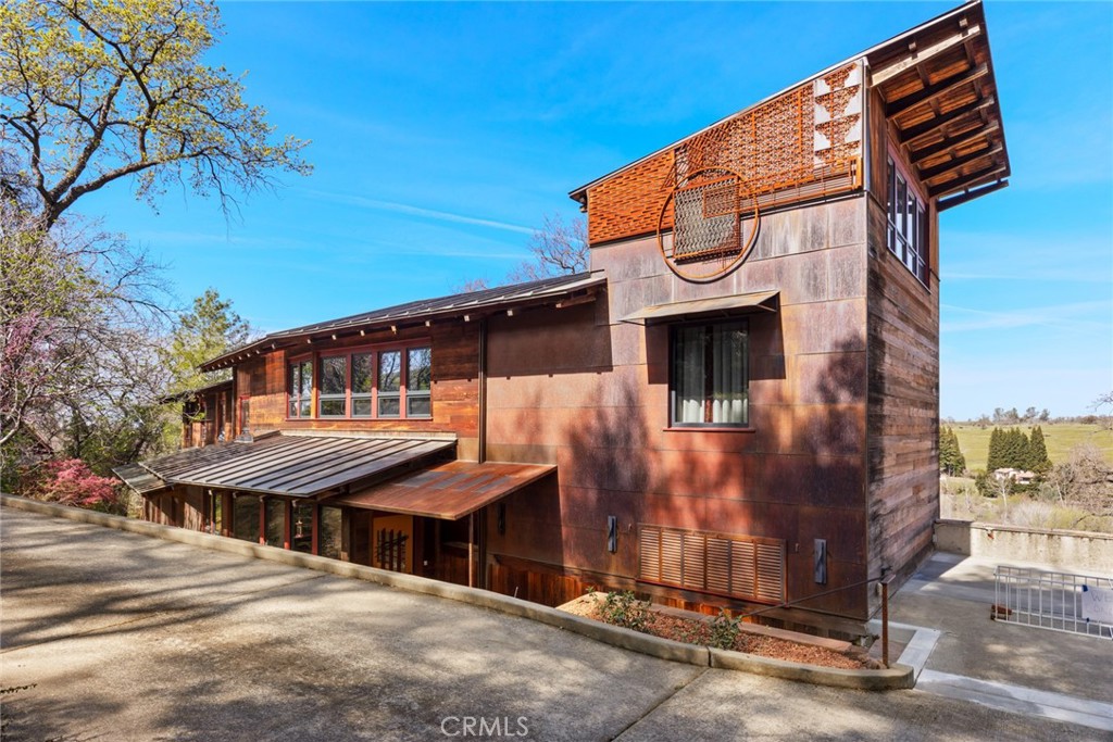 Welcome to this truly exceptional custom home nestled on 3 acres above Butte Creek. This 5-bed, 5-bath estate offers 3,733 sq ft of artfully crafted living space that blends seamlessly into its oak forest surroundings. Built in 1990 and thoughtfully updated throughout, this home is a rare combination of design, nature, and comfort. From the moment you arrive, you’re greeted by a detached garage featuring an EV charging station and a converted art studio, all perched above the main residence. The exterior is a masterpiece in itself, wrapped in redwood with a pure copper roof and owned solar for modern sustainability. Custom metalwork, Colorado flagstone paths, and a stunning walnut front door set the tone for the craftsmanship throughout the property. Inside, expansive windows and sliding doors draw you into panoramic views of the canyon, Butte Creek, and your private pool & spa. Natural light pours through skylights on both levels, enhancing the open and airy design. The heart of the home is a chef’s galley kitchen, fully remodel with custom Sapele wood cabinetry, dual dishwashers, a touchless faucet, 5-burner Zephyr electric stove, and an elegant bar, perfect for entertaining in style. All 5 bedrooms are located upstairs, w/ the primary offering breathtaking views, a spacious closet, and a spa-like bathroom. Enjoy the luxurious walk-in shower, double vanity w/ updated lighting, and heated towel racks—every detail considered for comfort. Additional interior features include a cozy wood-burning fireplace, large indoor laundry room, and split HVAC systems for year-round comfort. Step outside to experience a nature lover’s paradise. The two-lane lap pool includes a 66-foot swim lane for serious swimmers and a 10-foot “Margaritaville” section for relaxing—all set against canyon views and a sprawling flagstone deck for entertaining. There’s also a pool house, outdoor shower, and endless skies for stargazing. This property is also a haven for wildlife. Red-tailed hawks, herons, quail, owls, and even bald eagles make regular appearances. A resident osprey pair nests just below the home each spring. Located just minutes from Chico, the home offers the rare opportunity to live in luxurious harmony with nature. This home isn’t just a place to live—it’s a lifestyle, a sanctuary, and an experience.