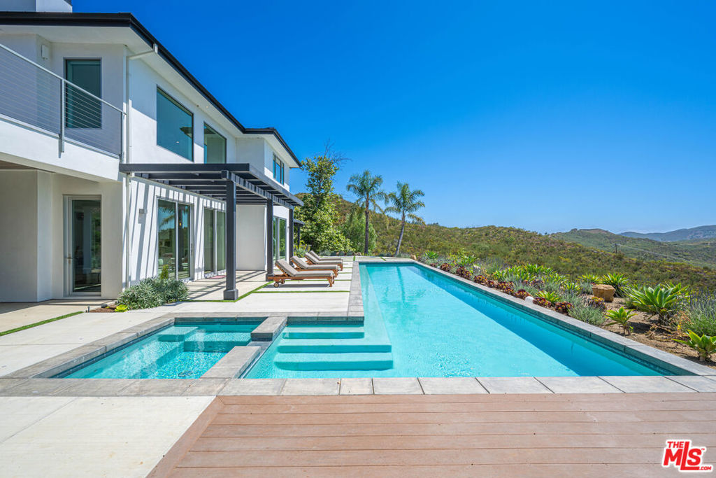 Available August 29. Discover unparalleled privacy, luxury, and natural splendor at this newly built, modern 4-bedroom, 4-bathroom estate sprawling across nearly 10 acres of tranquil Malibu countryside. Nestled behind a secure gated driveway, this architectural gem offers serenity and sophisticated living for the discerning homeowner. Panoramic mountain vistas envelop the property, showcased through soaring ceilings and expansive floor-to-ceiling windows with automated shades. The open-concept interior boasts elegant wood flooring and a bold custom concrete fireplace as its centerpiece. The chef's kitchen, outfitted with top-tier appliances and a generous pantry, seamlessly connects to an outdoor entertainment haven featuring a built-in BBQ, pizza oven, and ample dining space for gatherings. A dedicated den/movie room provides a cozy retreat for film nights. The primary suite is a haven of calm, complete with a spa-like bathroom, steam shower, and stunning views from a spacious upper deck. Two stylish guest suites reside upstairs, while a third, self-contained mini-suite occupies the main level. Outside, a glistening pool, spa, and infrared sauna are immersed in nature's quiet, accompanied only by birdsong and gentle breezes. Across the grounds, enjoy a lively bocce ball court and thriving vegetable garden. A two-car garage and robust Wi-Fi network enhance convenience. Ideal for stargazing or hosting memorable events, this extraordinary home delivers a lifestyle of peace, elegance, and seclusion you'll cherish forever.