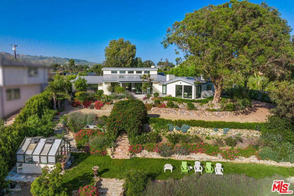 A sanctuary of privacy and open space with incredible sunsets and sweeping valley views, this reimagined contemporary ranch estate commands spectacular sunset vistas from high above Zuma Beach. The cul-de-sac property of over 2.9 acres is complete with a gorgeously updated home, two guest houses, a greenhouse, and grand expanses of flat and terraced landscaping with ample room for a pool, bocce, and ocean-view decks to enhance indoor-outdoor living and entertaining. A dramatic great room sits at the heart of the residence, with high ceilings, clerestory windows, skylights, wood floors, and huge glass doors opening to the back patio, pergola, and lush canyon and ocean views. This light-filled living/dining/kitchen space features a linear fireplace, handsome illuminated wood shelves and cabinets, and a spacious island kitchen with bar seating, breakfast area, and top-quality Miele appliances. To one side of the great room is a family/office/media room, plus a powder room. On the opposite wing of the single-level house are the home's three bedrooms, including a peaceful primary suite complete with a fireplace, a large closet, corner glass doors opening to the backyard, and a large, spa-style bath. The terraced backyard features a roomy pergola-shaded flagstone patio with a fireplace, rock-walled planter beds, beautiful mature trees, ocean-view sitting areas, a greenhouse, a giant outdoor chess board, an ocean-view guest house with kitchenette and full bath, and an art studio or activity room. The home has a two-car garage, a Tesla charger, an indoor-outdoor sound system, and air conditioning. A haven of Southern California beauty, away from it all, yet convenient to shopping, dining, and beaches.