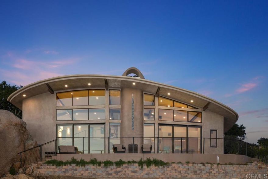 As recently featured in Dwell, an award-winning sustainable masterpiece envisioned by renowned architect Drew Hubbell of Hubbell & Hubbell. Perched at the edge of a canyon with panoramic views of the Pacific Ocean to the west and Palomar Mountain to the east. Hidden from the cul-de-sac below in Escondido’s iconic Boulder Landscape, this extraordinary “Museum of Imagination,” 3 bedroom, 4 bath custom home is harmoniously integrated into its natural surroundings of manzanita groves, native oaks, and massive granite boulders. Natural stone steps to the custom handcrafted entryway door you are  immersed in a property that lives in harmony with its surroundings. Inside, a soaring open-concept living space you’re greeted by its carefully curated light child- chandelier, sculptural curved staircase anchored by a natural interior boulder, a majestic wood-burning fireplace, and floor-to-ceiling glass doors and windows that frame breathtaking vistas. Every material was selected for sustainability, wellness, and longevity from polished concrete floors and bamboo cabinetry to natural stone accents and non-toxic custom finishes. The Kitchen features a curved island, energy-efficient appliances, a state-of-the-art induction cooktop, and smart oven. The living and dining areas enjoy dramatic views and abundant daylight, enhanced by operable clerestory windows and passive cross-ventilation. The primary suite captures tranquil canyon views and offers direct access to a private spa deck. Its ensuite bathroom feels like a retreat, with a curved walk-in tile shower, soaking tub, dual vanity, and bamboo cabinetry. The secondary loft-style bedroom offers expansive ocean and sunset views and each of the guest suites feature ensuite bathrooms and serene privacy. This Net-Zero home is powered by solar panels and includes mini-split HVAC systems, foam-core panel roofing, and ICCF walls made from post-consumer materials providing exceptional insulation, fire resistance, and durability. Deep overhangs and integrated interior boulders help regulate temperature and minimize energy use. The UV/Ozone spa system reduces chemical usage, while preserved native landscaping enhances the property's ecological integrity. Winner of the 2023 San Diego Green Building Council’s Maverick Award for Sustainable Leadership, and recognized by the County of San Diego’s Green Building Program. Just minutes from the exclusive Golden Door Resort, boutique wineries, the Escondido Center for the Arts, the world-famous Safari Park, and scenic local hiking trails, this location blends privacy with convenient access to the best of North County. San Diego—often celebrated as America’s Finest City—is a short drive away, with its world-class beaches, vibrant cultural scene, and year-round temperate climate.