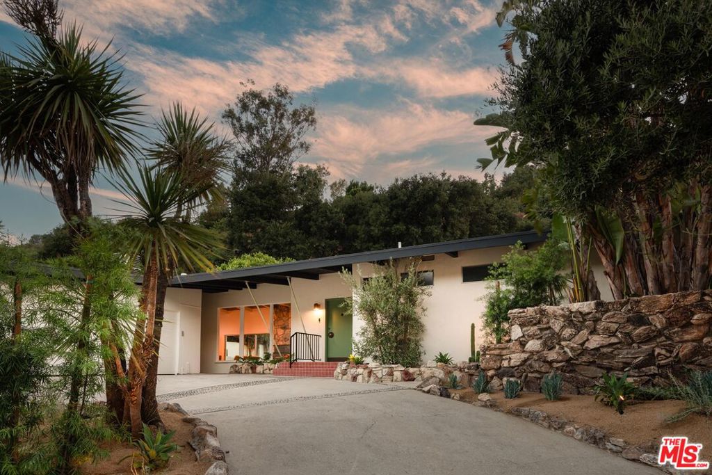 Originally designed in 1955 by esteemed architect Jack Chernoff, AIA, this masterfully reimagined mid-century residence embodies the timeless elegance and clean lines of its era, now thoughtfully tailored for contemporary living. Set against a backdrop of curated landscaping, this 3BD/2.5BA home offers an effortless blend of architectural integrity and modern refinement. Inside, light pours through expansive windows and sliding glass doors, highlighting the open floor plan and restored post-and-beam ceilings. Two distinct living areas, anchored by a dramatic original stone fireplace, create a seamless flow for both intimate gatherings and larger-scale entertaining. The kitchen, a true centerpiece, features striking black soapstone countertops, an oversized island, and custom cabinetry in a rich, rustic red, an unexpected and artful nod to vintage design. The primary suite includes a walk-in closet, built-in storage, and a spa-like en-suite bathroom adorned with a generous step-in shower draped in vibrant hand-selected tile. Two additional bedrooms, bathed in natural light, share a thoughtfully appointed bathroom with a dual vanity and refined finishes. A powder room and a dedicated laundry area conveniently located near the entry enhance the home's functionality. Take advantage of canyon views in the private backyard, complete with a deep original pool, multiple dining areas, and stunning landscaping. Every fixture and finish throughout the property has been carefully chosen to honor the home's architectural heritage while embracing the comfort and convenience of today. Ideally located just moments from Ventura Boulevard's vibrant dining and shopping scene, this exceptional residence is a rare fusion of design pedigree, modern sophistication, and iconic California indoor-outdoor living.