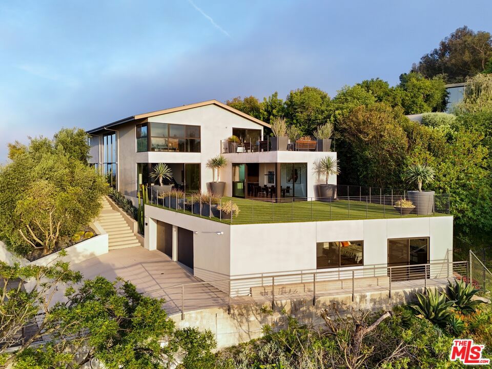 Tucked away on a beloved, private road where turnover is low and some residents own multiple homes, this fantastic refuge promises riveting panoramic views at every moment and peaceful comfort above it all. From sunrise to sunset and into calm California nights, unobstructed vistas inspire creative thought and invoke a passion for this rare way of life in harmony with its natural surround. Sited up a long private driveway with parking for numerous vehicles, the home is meticulously appointed with beautiful drought-tolerant landscaping including whimsical olive trees and carefully curated cacti. Guests arrive through a pivot door as floor-to-ceiling panes of glass welcome natural light into the double-height foyer. Entertain in style with a seamless indoor-outdoor vibe as pocket doors fully retract in the living room to provide a casual, elegant flow from east to west. A state-of-the-art Arclinea kitchen is equipped with Miele ovens and appliances as well as a Wolf cooktop, custom Sub-Zero refrigerator, and a generous waterfall island with breakfast bar ledge. The nearby formal dining room, also with retreating doors, is appointed with an impressive floating wall close-off to add intimacy to parties and guide the movement of attendees. Upstairs, the primary suite is magnificent, complete with a sumptuous bath with floating dual-sink vanity, separate shower, toilet room, and centerpiece soaking tub aside walls of sliding glass that open to reveal a private patio with fire pit. A large walk-in closet has custom built-ins to please any modern fashionista. Secondary bedrooms showcase striking mountain and valley views, and bathrooms are dressed in white Italian lacquer cabinets topped in soothing gray Silestone. Screen films in the media room with its plush double-pad cushy floor, or work and study in the roomy office with built-ins and picture window. Downstairs, discover a spacious guest quarters with private entrance and direct access to the home's expansive driveway and motor court. Here, a variety of possibilities and configurations abound, from yoga, massage, and wellness to a potential recording studio or artist's haven! Complete with en-suite bath, separate HVAC, and walk-in closet, this partitioned space can also be utilized for passive income. Outside, there are multiple lawns, a saltwater pool and spa, and a sprawling lounging deck from which the back of the Hollywood Sign's H can be seen as well as the San Jacinto Mountains 100+ miles away! Enjoy close proximity to hiking trails including Dixie Canyon Park, centrally located just moments to the high fashion of Rodeo Drive or the boutique charm of Studio City. Welcome to a fresh, coveted lifestyle relished from this singular viewpoint in a world-famous locale just off of Mulholland Drive. Also available fully furnished, including most of the artwork (negotiable; inquire for details).