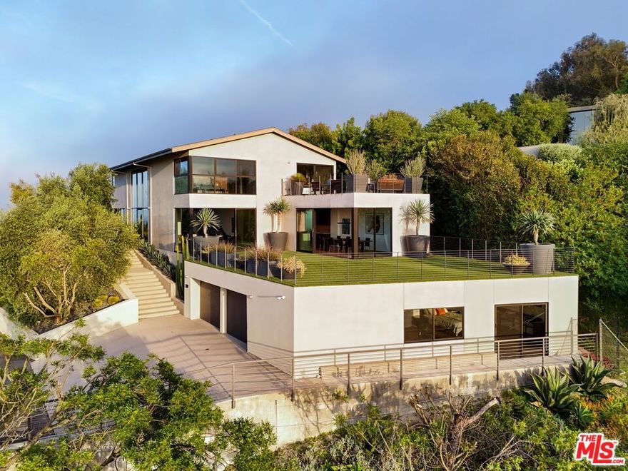 Tucked away on a beloved, private road where turnover is low and some residents own multiple homes, this fantastic refuge promises riveting panoramic views at every moment and peaceful comfort above it all. From sunrise to sunset and into calm California nights, unobstructed vistas inspire creative thought and invoke a passion for this rare way of life in harmony with its natural surround. Sited up a long private driveway with parking for numerous vehicles, the home is meticulously appointed with beautiful drought-tolerant landscaping including whimsical olive trees and carefully curated cacti. Guests arrive through a pivot door as floor-to-ceiling panes of glass welcome natural light into the double-height foyer. Entertain in style with a seamless indoor-outdoor vibe as pocket doors fully retract in the living room to provide a casual, elegant flow from east to west. A state-of-the-art Arclinea kitchen is equipped with Miele ovens and appliances as well as a Wolf cooktop, custom Sub-Zero refrigerator, and a generous waterfall island with breakfast bar ledge. The nearby formal dining room, also with retreating doors, is appointed with an impressive floating wall close-off to add intimacy to parties and guide the movement of attendees. Upstairs, the primary suite is magnificent, complete with a sumptuous bath with floating dual-sink vanity, separate shower, toilet room, and centerpiece soaking tub aside walls of sliding glass that open to reveal a private patio with fire pit. A large walk-in closet has custom built-ins to please any modern fashionista. Secondary bedrooms showcase striking mountain and valley views, and bathrooms are dressed in white Italian lacquer cabinets topped in soothing gray Silestone. Screen films in the media room with its plush double-pad cushy floor, or work and study in the roomy office with built-ins and picture window. Downstairs, discover a spacious guest quarters with private entrance and direct access to the home's expansive driveway and motor court. Here, a variety of possibilities and configurations abound, from yoga, massage, and wellness to a potential recording studio or artist's haven! Complete with en-suite bath, separate HVAC, and walk-in closet, this partitioned space can also be utilized for passive income. Outside, there are multiple lawns, a saltwater pool and spa, and a sprawling lounging deck from which the back of the Hollywood Sign's H can be seen as well as the San Jacinto Mountains 100+ miles away! Enjoy close proximity to hiking trails including Dixie Canyon Park, centrally located just moments to the high fashion of Rodeo Drive or the boutique charm of Studio City. Welcome to a fresh, coveted lifestyle relished from this singular viewpoint in a world-famous locale just off of Mulholland Drive. Also available fully furnished, including most of the artwork (negotiable; inquire for details).