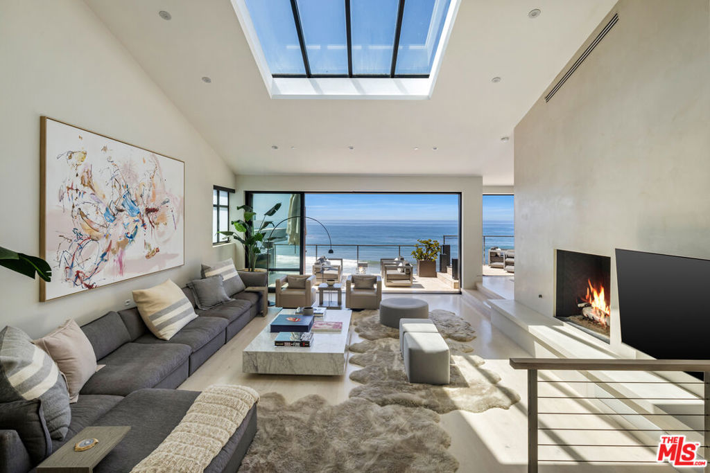 Set at the end of a private cul-de-sac on an ultra-exclusive gated street just off Broad Beach Road, this extraordinary Malibu residence offers a rare combination of seclusion, architecture, and panoramic oceanfront living. Set above the sand in one of Malibu's most coveted coves, the property unfolds in layers beginning with a tranquil entry garden and outdoor lounge that immediately sets a tone of intimacy and retreat. Behind the gate, the reimagined contemporary beach house spans four bedrooms and six thoughtfully designed bathrooms across multiple light-filled levels, all accessed by elevator and fully integrated into a state-of-the-art smart home system. From the moment of entry, the ocean view foyer hints at the scale and intention of the interiors: tray ceilings with soffit lighting, dramatic skylights, and sky-high volumes that usher in golden daylight. Expanses of French oak flooring guide the flow through a series of grand entertaining spaces including a dramatic formal living room with soaring double-height ceilings, an oceanfront dining area framed by disappearing walls of glass, and generous outdoor decks that capture unobstructed views of the coastline, Catalina, and every sunset in between. A separate ocean-facing family room doubles as a bar and lounge space, complete with fireplace, while the main living areas open to an expansive terrace equipped for full-day enjoyment a built-in outdoor kitchen, barbecue, fire pit, flatscreen television, and plenty of seating for open-air dining or movie nights by the sea. The chef's kitchen is enveloped in Calacatta marble and backdropped by endless blue sea, appointed with professional-grade stainless steel appliances. An additional entertaining level is dedicated to leisure, with a plush media room anchored by a wine showcase wall, a full bar, and lounge seating all flowing out to a lower terrace featuring a spa and sundeck. A private guest suite on this level offers a luxuriously appointed bath and sliding glass doors with direct access to the sandy beaches below. The primary suite is a study in beachfront serenity, elevated to maximize the view and designed to evoke a personal retreat. A wall of glass offers uninterrupted sight lines to the cove beyond, while the ensuite bath featuring dual vanities, walk-in closets, and a soaking tub positioned to overlook the shoreline brings spa-level luxury into everyday living. Additional amenities include a dedicated wellness loft with massage and exercise space, a library, and an upstairs office/bonus area framed by vaulted ceilings and skylights, offering an inspiring perch above the main living areas. Outdoor moments continue throughout the home, from private bedroom balconies to layered garden terraces and expansive decks that seamlessly extend each interior space into the sun and sea air. Meticulously reimagined and designed for both privacy and presence, this coastal sanctuary delivers the ultimate in contemporary Malibu living.