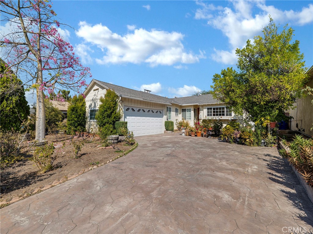 Welcome to this beautifully maintained Tarzana residence offering 3 spacious bedrooms and 2 bathrooms. The landscaped front yard features a rose garden and fruit trees, creating a warm and inviting curb appeal. Inside, the front door opens to a large living and dining room combination highlighted by a cozy corner fireplace and rich wood flooring that adds warmth throughout. The updated galley kitchen boasts newer cabinets, granite countertops, and a convenient pantry and laundry area just off to the side. The layout provides privacy with two bedrooms and one bath on one side of the home, and an additional bedroom with bath on the other. All bedrooms are generously sized with ample closet space, and one bathroom has been tastefully updated. Sliding doors from the main living area lead to a serene and private backyard retreat. Enjoy a spacious covered patio with stamped concrete, low-maintenance artificial turf, a tranquil waterfall feature, and mature trees—perfect for entertaining or relaxing. Additional highlights include an attached two-car garage, a stamped driveway, and close proximity to Ventura Blvd, dining, shopping, and freeway access.