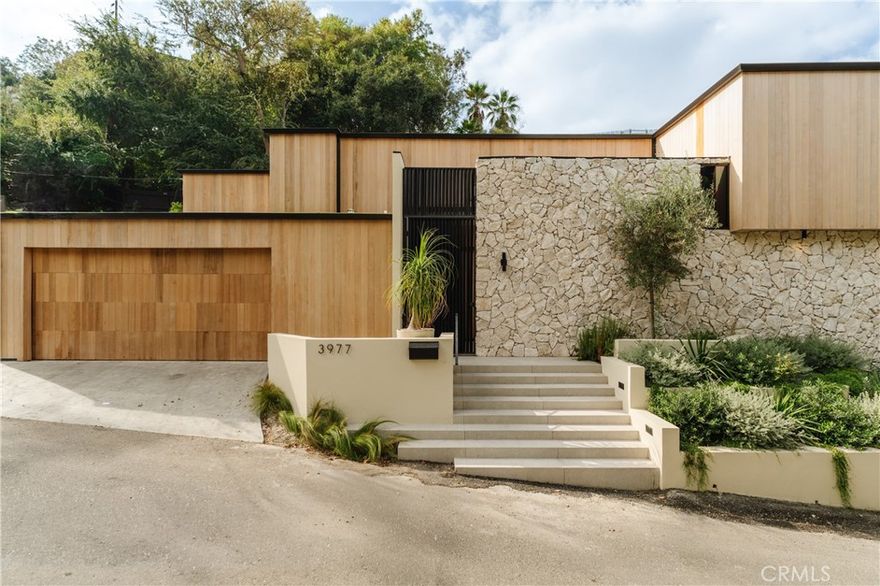 This strikingly reimagined mid-century residence, privately set south of the Boulevard in coveted Studio City. Every inch of this 3-bedroom, 2.5-bath home with an additional office reflects refined craftsmanship, natural warmth, and modern design. The exterior immediately captivates with rich cedar cladding and hand-laid stonework, setting the tone for the sophisticated interiors within. Inside, airy open spaces unfold across herringbone-patterned wood floors, framed by custom millwork and natural textures that evoke a sense of calm and connection. The heart of the home is the seamless living, dining, and kitchen area — bright, inviting, and designed for effortless entertaining. Floor-to-ceiling glass doors extend the space outward to a private patio with a built-in grill, perfect for gathering or relaxing under the California sun. The chef’s kitchen impresses with white oak cabinetry, Viola Monet Calacatta marble, paneled appliances, and sleek fixtures — blending organic materials with contemporary elegance. A powder room, laundry area, and attached two-car garage with EV charger complete the main level. Upstairs, the tranquil primary suite is a modern sanctuary with expansive windows, custom closets, and a spa-inspired bath featuring a soaking tub, walk-in shower, and dual vanities. Two additional bedrooms, a full bath, and a flexible den or office provide comfort and versatility for family or guests. Tucked in one of Studio City’s most desirable pockets, this home offers easy access to hiking trails, Mulholland Drive, Beverly Hills, and The Shops at Sportsmen’s Lodge — with Erewhon, Equinox, and top dining just minutes away. A private, polished retreat that embodies elevated California living.
