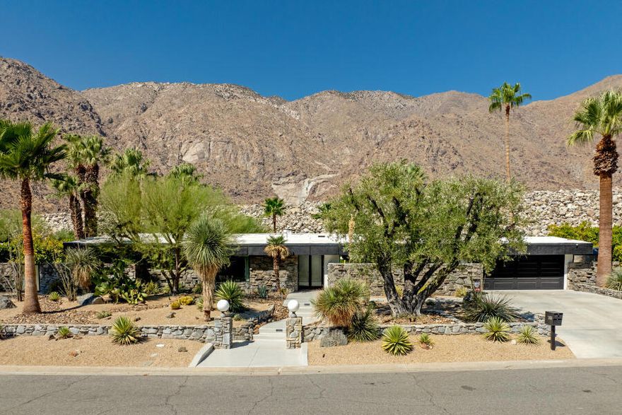 The most exquisite Midcentury Modern home ever available in Vista Las Palmas has come to market for the most discerning buyer. Originally built by the famed Alexander Company and renovated by Christopher Kennedy for the Palm Springs Modernism Tour, this architectural gem blends timeless design with luxurious modernism. The home welcomes you with an expansive open floor plan featuring a dramatic floor-to-ceiling marble fireplace, exposed beam ceilings, and Cantina-style hideaway doors. These seamlessly connect the living and dining areas to a stunning poolside courtyard, showcasing views of the San Jacinto Mountains directly behind the home.The main living area is spacious with a gas fireplace. Adjacent is the dining space with a handcrafted wood table that comfortably seats eight and opens to a chef's kitchen. The striking marble center island doubles as prep space and includes bar seating for two. Large windows flood the kitchen with natural light and frame views of the Las Palmas neighborhood. Five bedrooms offer luxury accommodations, including four in the main house and one in the attached guest casita. The primary suite, located on the west side of the home, features sliding glass doors opening to the serene backyard. Its spa-inspired ensuite includes a dual-sink vanity, oversized walk-in shower, stand-alone soaking tub, and sliding doors leading to a private garden with a walk-in closet.On the opposite wing are three additional bedrooms and a second master suite with direct pool access through sliding doors. This suite features ample closet space luxurious marble bathroom with an oversized shower, dual rain heads. The additional two guest rooms share a well-appointed bathroom with a single vanity and glass-enclosed shower.The fifth bedroom, located in an attached guest casita, offers ultimate privacy. It includes a private entrance, mini-fridge, its own A/C unit, and an ensuite bath with a glass-panel shower and single vanity. The backyard is a true showstopper. Set against a mountain backdrop, the sparkling pool and spa are surrounded by lush landscaping and resort-style amenities including a 3-hole mini putting green, out door shower, six loungers, a bocce court, shaded dining area for eight, gas barbecue, and firepit. Furniture, accessories and artwork is available for purchase outside of escrow.  For the first time in months Vista Las Palmas is available for Short Term Rentals, this is a very successful high-end rental property.