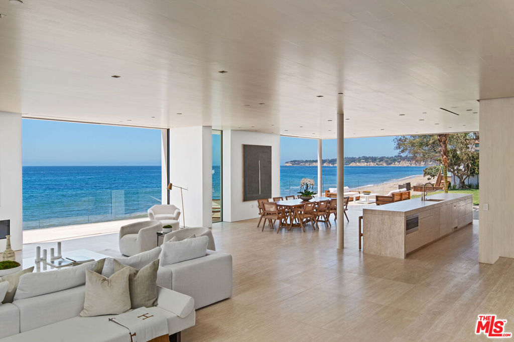 Truly extraordinary, cannot be reproduced, one-of-a-kind architectural, located on two separate legal parcels on a private road with 130 feet of beach frontage. This spacious and luxurious residence commands coastline, island, and ocean views from Point Dume to Palos Verdes. With the visionary design of international architect Chad Oppenheim along with Doug Burdges office providing local architecture planning, the sleek structure is a study in serenity: Venetian plaster, rift sawn white oak, enormous vanishing pocket doors, Navona travertine floors, and a generous open layout for effortless indoor-outdoor living and entertaining. The three levels are served by an elevator as well as a stunning illuminated spiral staircase with the elegance of a nautilus shell. Gated and very private, the homes main entrance is set in a tranquil landscaped courtyard, with the large pivoting glass front door offering the first of many striking sightlines. The main floor comprises an open living, dining, and kitchen area with high rift sawn oak ceilings and absolutely remarkable views from wraparound windows and doors that open seamlessly to the oceanfront deck and patio. The two-level living area features a fireplace, gallery walls, and two large seating areas, one open to the ocean, the other open to a very private outdoor garden living room with a 20-foot-long fireplace and a large Italian-marble fountain. The dining area is open to the deck, where there is additional seating and ample room for entertaining and al fresco dining. There are two kitchens: one adjacent to the dining area, with a long island, bar seating, beautiful oak cabinets, and Wolf and Miele appliances, the other up a few steps, equipped for the most ambitious gourmet entertaining with another range, dual ovens and dishwashers, and pantry cabinets. A beautiful Italian travertine powder room and an indoor/outdoor shower room complete the main floor. On the upper floor, there is another living room, this one with a glass ceiling and wood beams. A wall of glass at one end of the room opens to a large outdoor living area with sparkling ocean views. The four en-suite ocean-view bedrooms on this level, all with beautiful rift sawn oak floors, ceilings, and cabinets, include two sensational owners suites with sitting areas, custom closets, and magnificent spa-style travertine bathrooms. The lowest level is home to a temperature-controlled wine storage display wall, a fully- equipped media room, plus a laundry room and powder room. The property has room for a guest house (under construction) or additional home and an oceanfront swimming pool next to an expansive lawn and 100-year-old Olive Grove. There is a two-car garage with guest parking for 14 cars and the property is beautifully landscaped, with drip irrigation, landscape lighting, steps to the beach, palms, and century-old olive trees. Smart-home features include camera security, automated shades, and multizone air conditioning. This is truly a remarkable beach estate for a lifestyle of uncommon luxury.Includes 27234 PCH - APN# 4460-028-016 and 27242 PCH - APN# 4460-028-003.