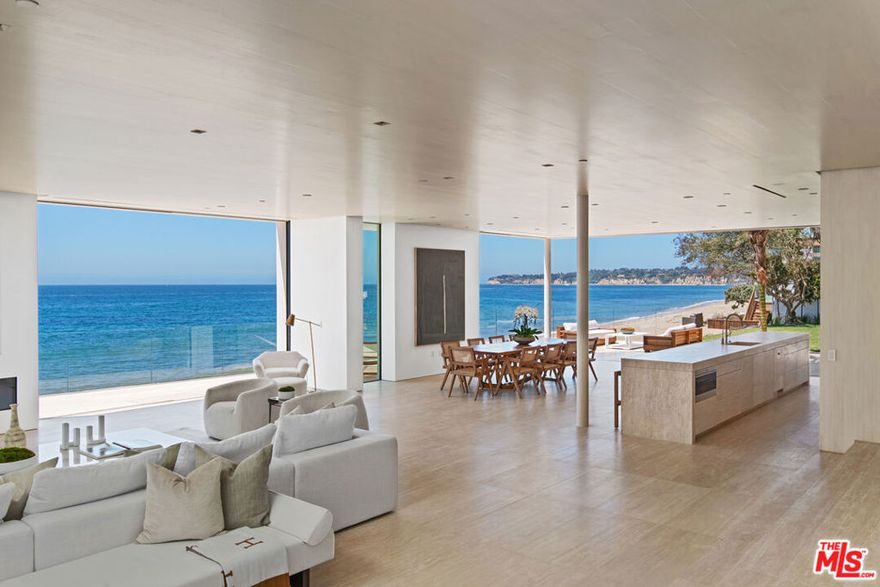 Truly extraordinary, cannot be reproduced, one-of-a-kind architectural, located on two separate legal parcels on a private road with 130 feet of beach frontage. This spacious and luxurious residence commands coastline, island, and ocean views from Point Dume to Palos Verdes. With the visionary design of international architect Chad Oppenheim along with Doug Burdges office providing local architecture planning, the sleek structure is a study in serenity: Venetian plaster, rift sawn white oak, enormous vanishing pocket doors, Navona travertine floors, and a generous open layout for effortless indoor-outdoor living and entertaining. The three levels are served by an elevator as well as a stunning illuminated spiral staircase with the elegance of a nautilus shell. Gated and very private, the homes main entrance is set in a tranquil landscaped courtyard, with the large pivoting glass front door offering the first of many striking sightlines. The main floor comprises an open living, dining, and kitchen area with high rift sawn oak ceilings and absolutely remarkable views from wraparound windows and doors that open seamlessly to the oceanfront deck and patio. The two-level living area features a fireplace, gallery walls, and two large seating areas, one open to the ocean, the other open to a very private outdoor garden living room with a 20-foot-long fireplace and a large Italian-marble fountain. The dining area is open to the deck, where there is additional seating and ample room for entertaining and al fresco dining. There are two kitchens: one adjacent to the dining area, with a long island, bar seating, beautiful oak cabinets, and Wolf and Miele appliances, the other up a few steps, equipped for the most ambitious gourmet entertaining with another range, dual ovens and dishwashers, and pantry cabinets. A beautiful Italian travertine powder room and an indoor/outdoor shower room complete the main floor. On the upper floor, there is another living room, this one with a glass ceiling and wood beams. A wall of glass at one end of the room opens to a large outdoor living area with sparkling ocean views. The four en-suite ocean-view bedrooms on this level, all with beautiful rift sawn oak floors, ceilings, and cabinets, include two sensational owners suites with sitting areas, custom closets, and magnificent spa-style travertine bathrooms. The lowest level is home to a temperature-controlled wine storage display wall, a fully- equipped media room, plus a laundry room and powder room. The property has room for a guest house (under construction) or additional home and an oceanfront swimming pool next to an expansive lawn and 100-year-old Olive Grove. There is a two-car garage with guest parking for 14 cars and the property is beautifully landscaped, with drip irrigation, landscape lighting, steps to the beach, palms, and century-old olive trees. Smart-home features include camera security, automated shades, and multizone air conditioning. This is truly a remarkable beach estate for a lifestyle of uncommon luxury.Includes 27234 PCH - APN# 4460-028-016 and 27242 PCH - APN# 4460-028-003.