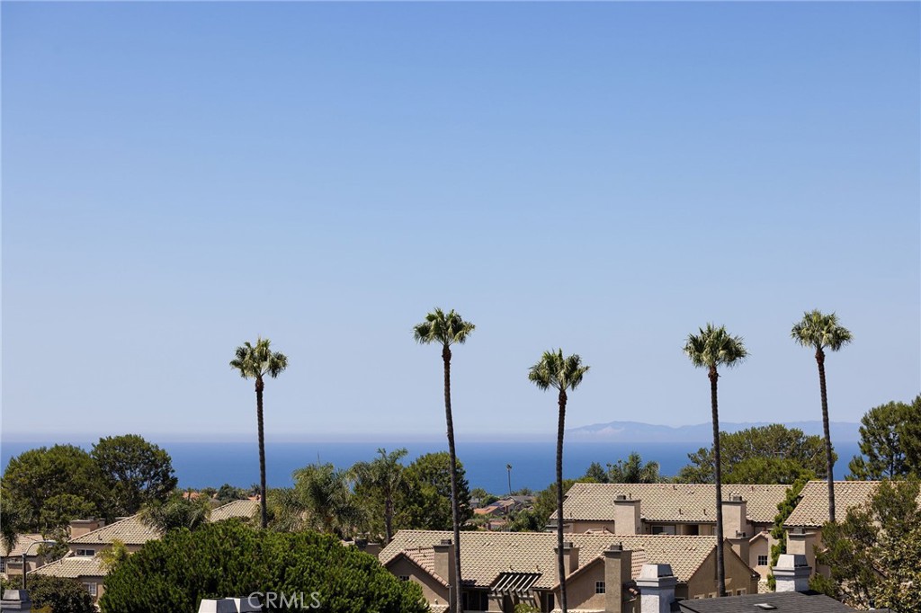 Experience elevated Dana Point coastal living in the exclusive gated community of Encantamar, where ocean views and sunset colors are your daily backdrop. This single-level home features a flowing, open concept with two bedrooms, two full baths, and extensive updates throughout, all oriented to enjoy the coastline and evening skies. Arrive to your private two-car garage with electric vehicle charging outlet and plenty of guest parking nearby. Inside, a formal foyer opens to light-filled living and dining areas with a custom fireplace and sliding doors to a view deck. A bar nook and outdoor living space make entertaining simple, and the southwest exposure frames nightly color over the water. Wide-plank floors guide you through the designer chef's kitchen, featuring quartz countertops, crisp white cabinetry, subway-tile backsplash, and stainless-steel appliances. Vaulted ceilings create an airy atmosphere in the eat-in breakfast nook and convenient quartz built-in desk, while skylights bathe the space in natural light. Both bathrooms have also been remodeled with elegant quartz finishes and upgraded fixtures. The thoughtful floor plan places the two bedrooms on opposite sides for maximum privacy and flexibility. The first spacious bedroom features vaulted ceilings, a large window with plantation shutters, and a generous walk-in closet. The primary suite serves as a private retreat, complete with a sitting area that captures stunning views, plus an upgraded en-suite bath with a double-sink vanity and large walk-in closet. Convenient in-unit laundry is located nearby. Located in the highly desired Encantamar community, you'll enjoy walking distance to shopping, dining, and theaters, with Dana Point Harbor, beaches, and the 5 freeway just minutes away. Community amenities include a year-round heated pool, spa, clubhouse, and fitness center. This is coastal living at its best, offering the complete package of views, location, and community lifestyle.
