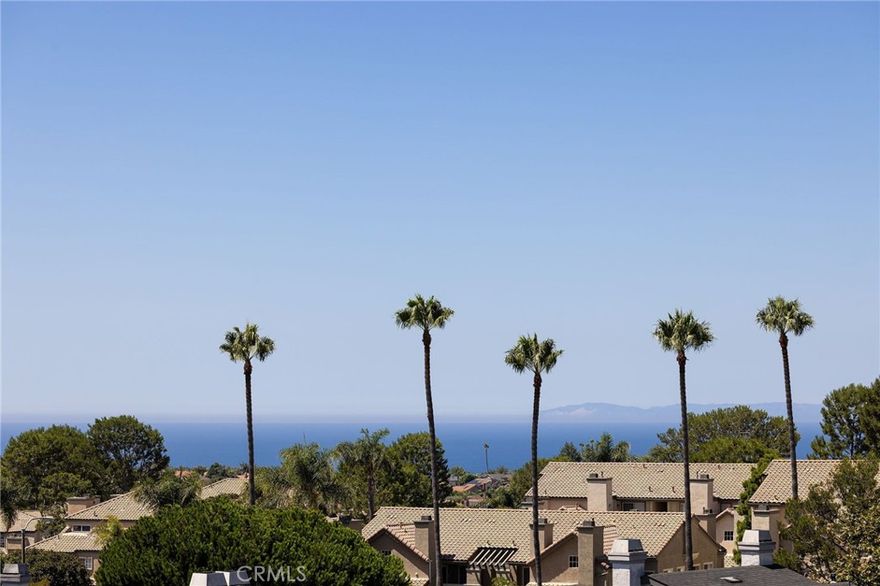 Experience elevated Dana Point coastal living in the exclusive gated community of Encantamar, where ocean views and sunset colors are your daily backdrop. This single-level home features a flowing, open concept with two bedrooms, two full baths, and extensive updates throughout, all oriented to enjoy the coastline and evening skies. Arrive to your private two-car garage with electric vehicle charging outlet and plenty of guest parking nearby. Inside, a formal foyer opens to light-filled living and dining areas with a custom fireplace and sliding doors to a view deck. A bar nook and outdoor living space make entertaining simple, and the southwest exposure frames nightly color over the water. Wide-plank floors guide you through the designer chef's kitchen, featuring quartz countertops, crisp white cabinetry, subway-tile backsplash, and stainless-steel appliances. Vaulted ceilings create an airy atmosphere in the eat-in breakfast nook and convenient quartz built-in desk, while skylights bathe the space in natural light. Both bathrooms have also been remodeled with elegant quartz finishes and upgraded fixtures. The thoughtful floor plan places the two bedrooms on opposite sides for maximum privacy and flexibility. The first spacious bedroom features vaulted ceilings, a large window with plantation shutters, and a generous walk-in closet. The primary suite serves as a private retreat, complete with a sitting area that captures stunning views, plus an upgraded en-suite bath with a double-sink vanity and large walk-in closet. Convenient in-unit laundry is located nearby. Located in the highly desired Encantamar community, you'll enjoy walking distance to shopping, dining, and theaters, with Dana Point Harbor, beaches, and the 5 freeway just minutes away. Community amenities include a year-round heated pool, spa, clubhouse, and fitness center. This is coastal living at its best, offering the complete package of views, location, and community lifestyle.